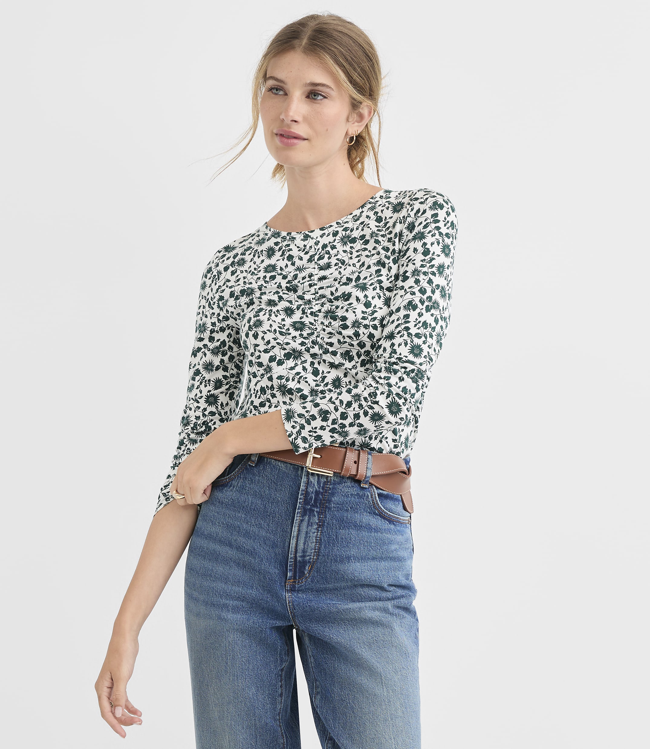 A woman in a floral top and jeans stands against a plain white background.