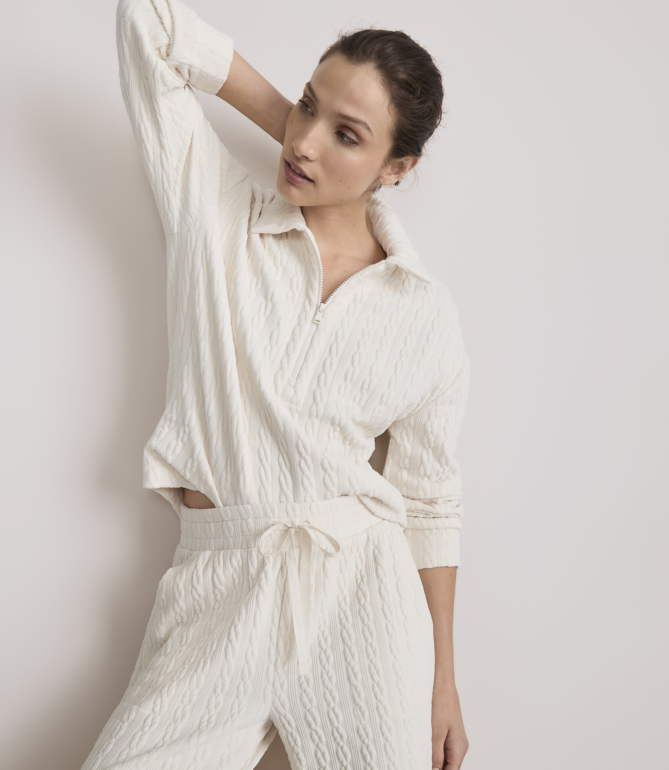 A woman in a cream-colored cable-knit loungewear set poses against a plain white background.