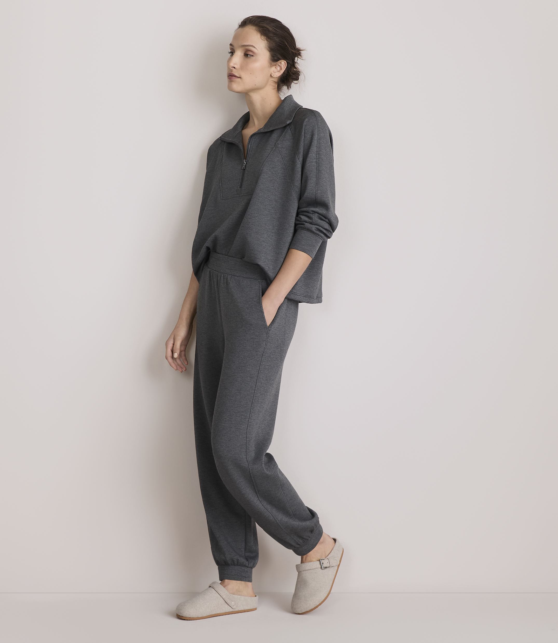 A woman in a grey loungewear set stands against a plain, light-colored wall.