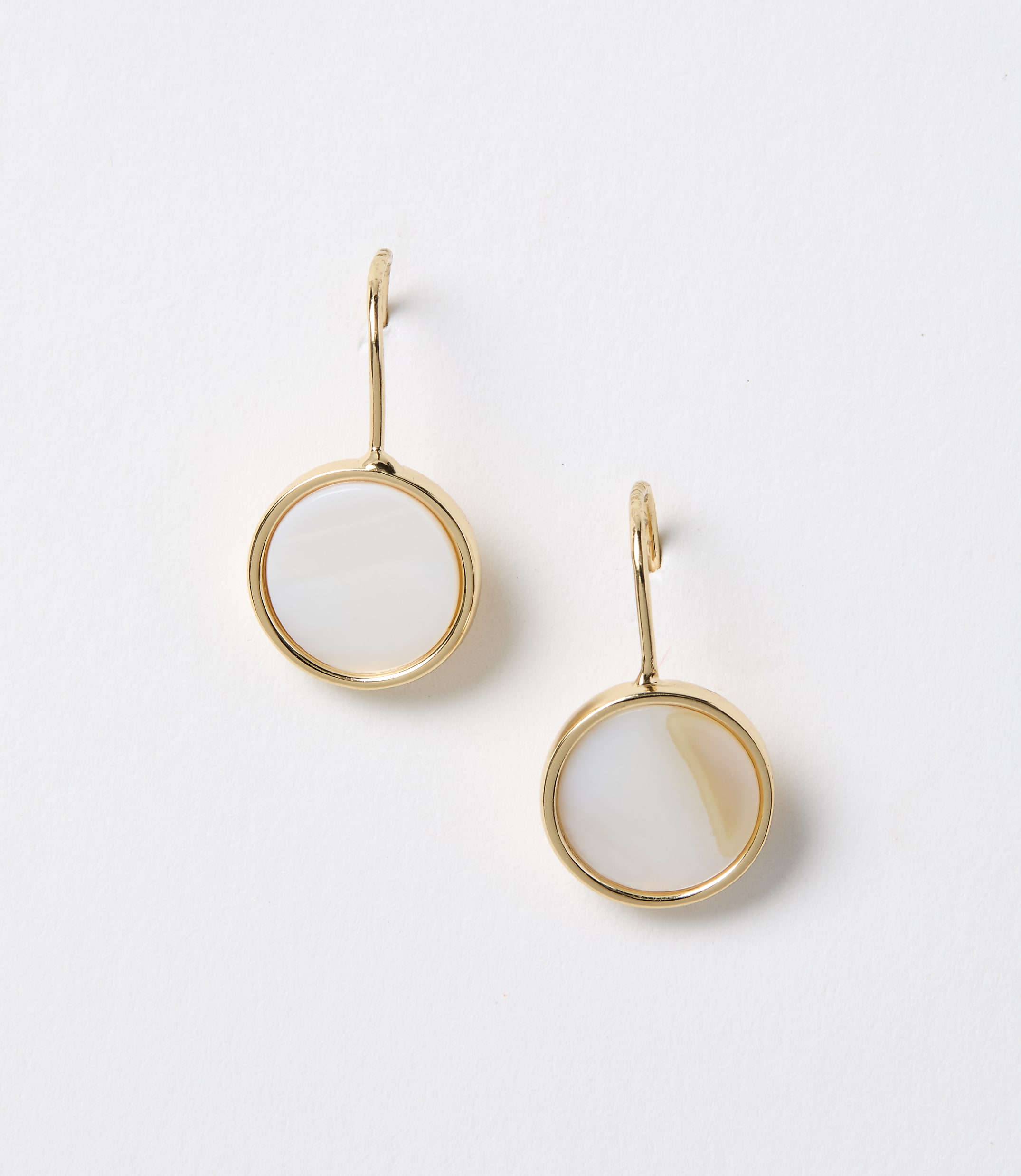 A pair of gold-rimmed circular mother-of-pearl earrings hang against a plain white background.