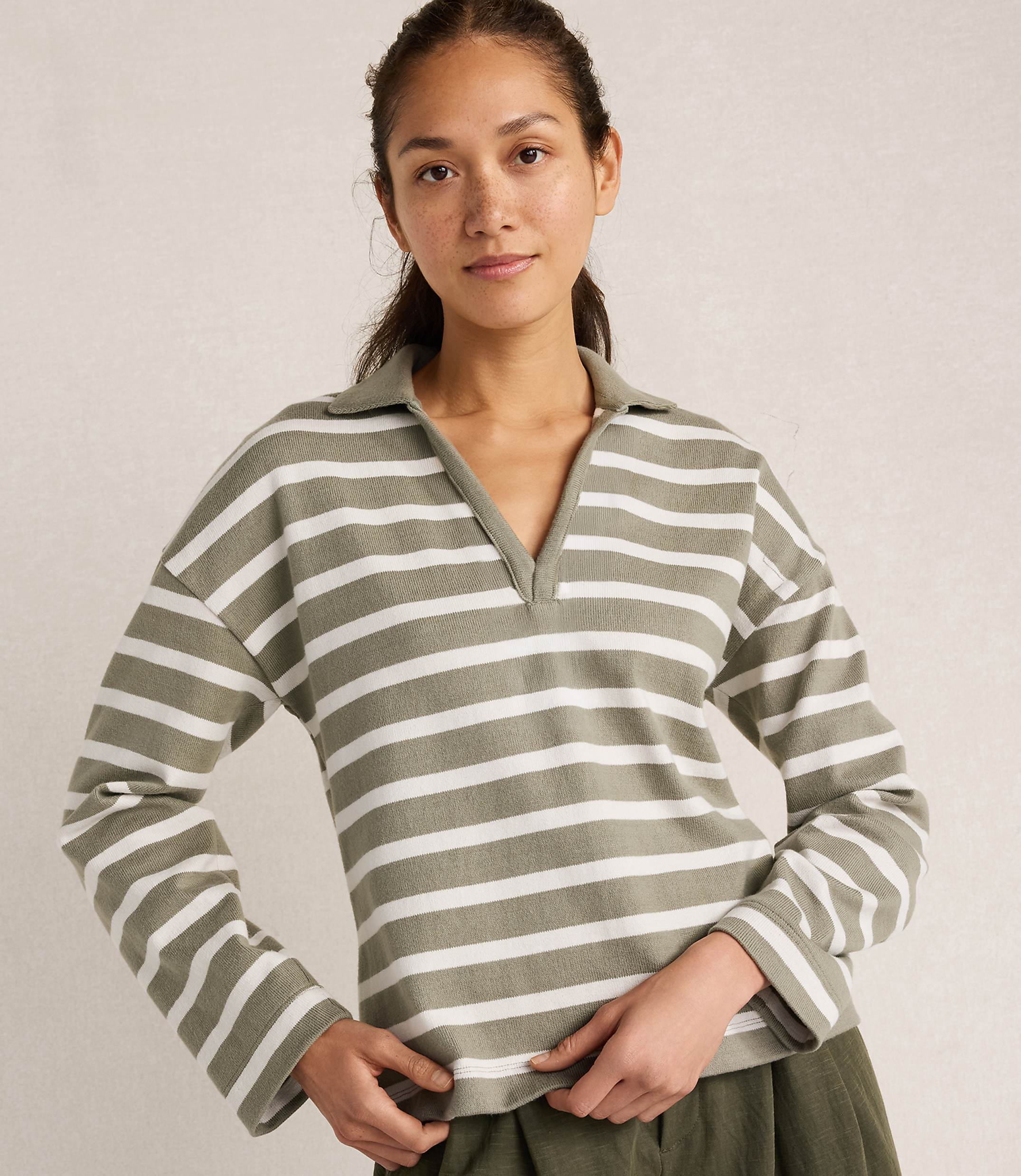 A woman in a striped shirt stands against a plain, light-colored background.