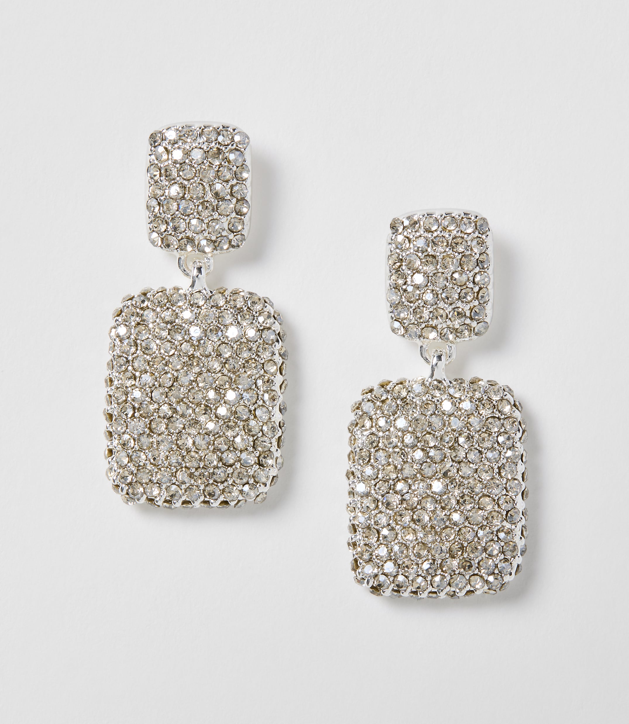 A pair of dazzling, rectangular, rhinestone-encrusted drop earrings hang against a plain white background.