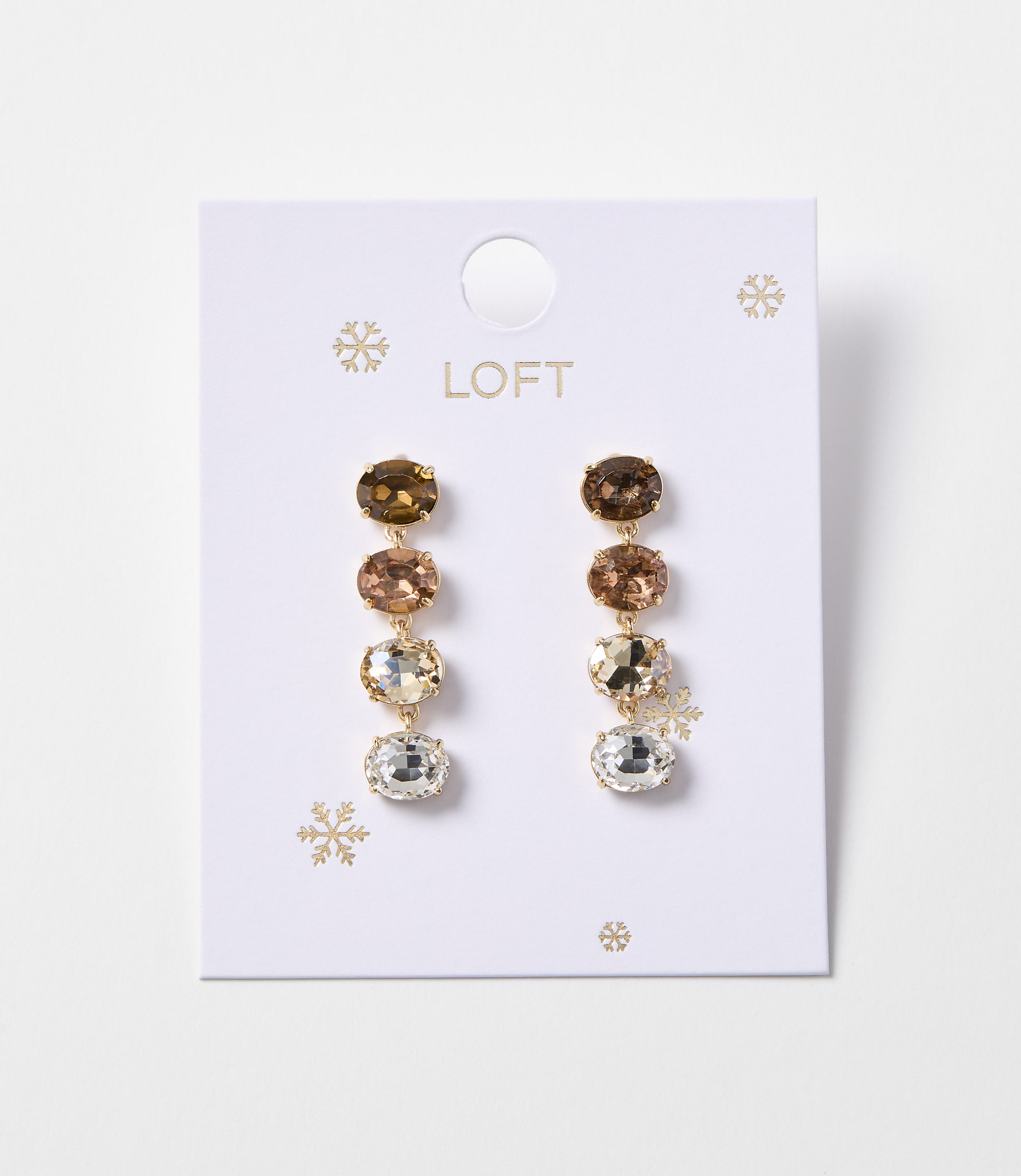 A pair of gold drop earrings with four oval-shaped gemstones in varying shades of brown and clear are displayed on a white card with snowflake accents and the "LOFT" logo.