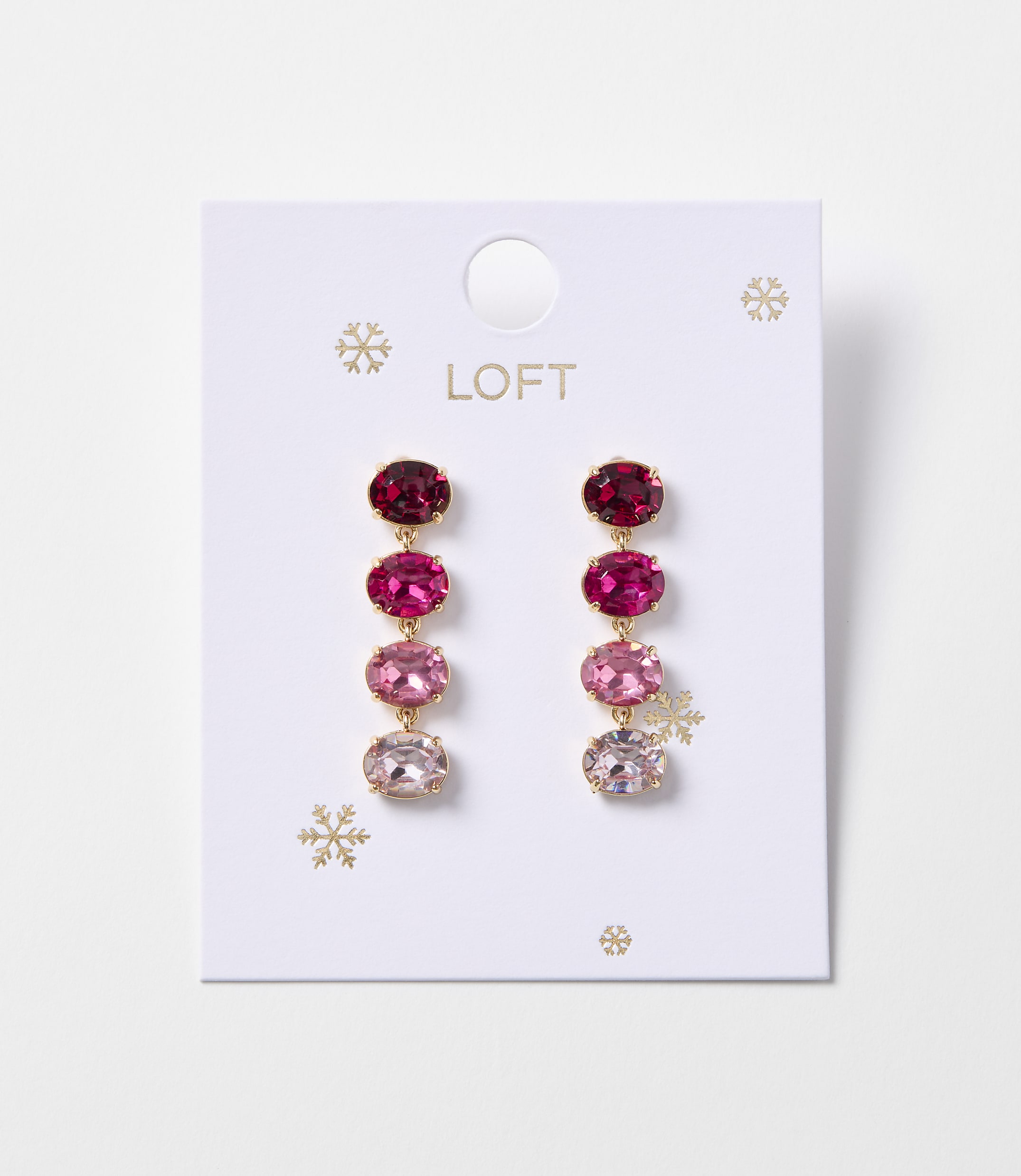 A pair of oval gemstone drop earrings in shades of pink and red hang from a white card with snowflake accents.