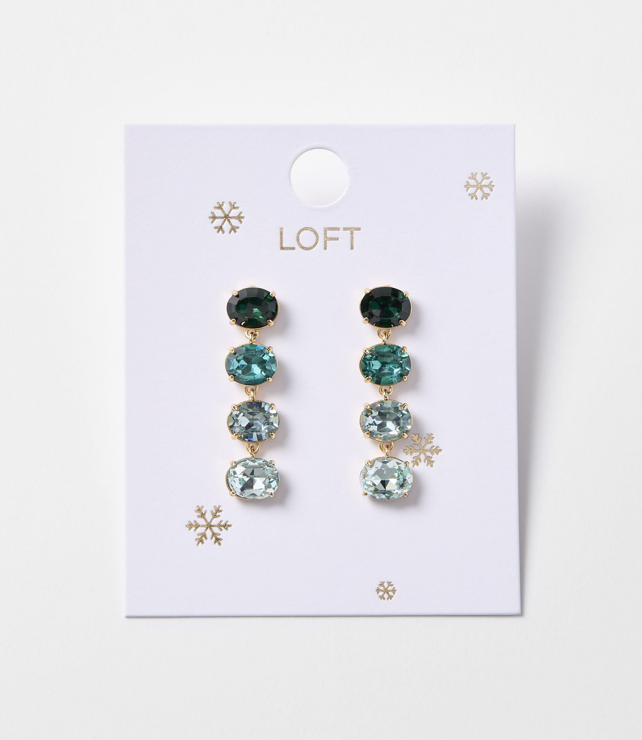 A pair of oval gemstone drop earrings in shades of green and blue hang from a white Loft card adorned with snowflakes.