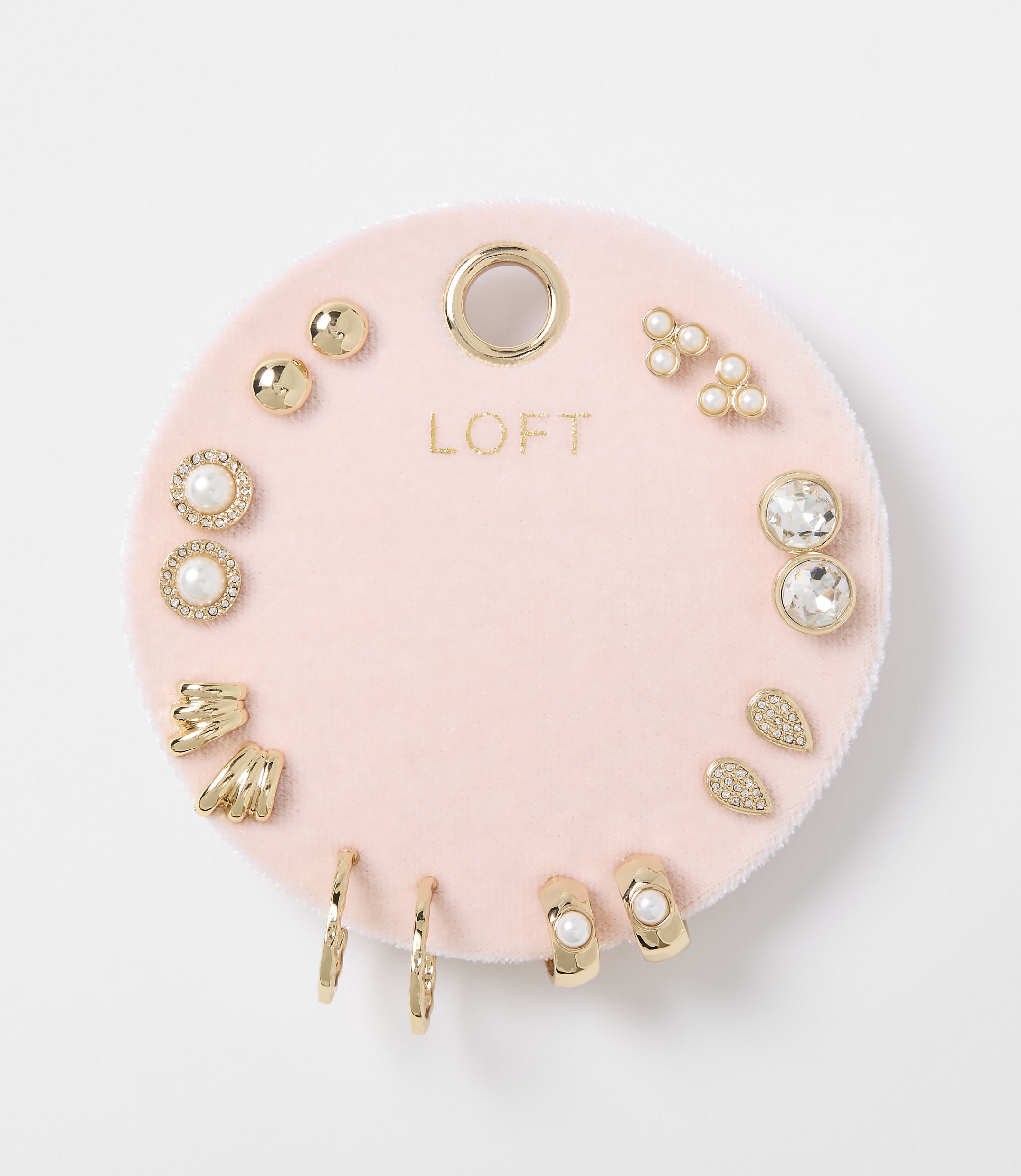 A collection of gold and pearl earrings are displayed on a pink velvet card against a white background.