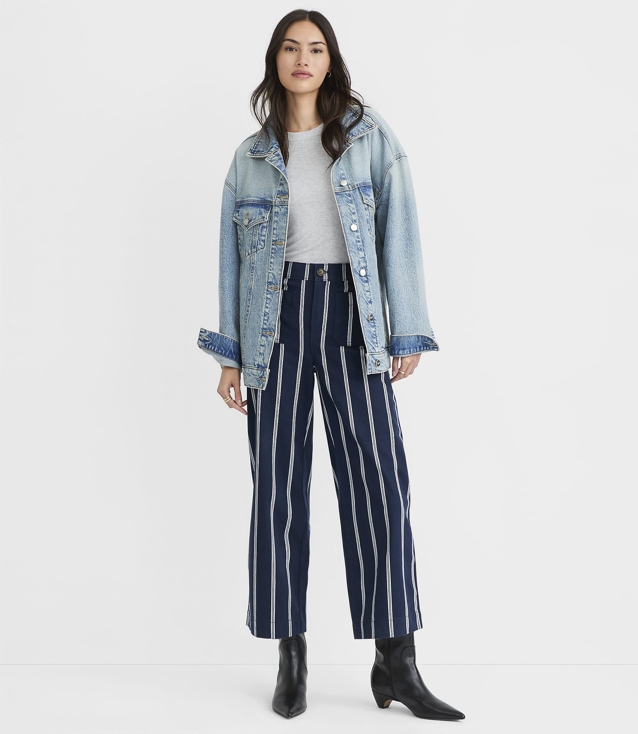 A woman in a denim jacket and striped pants stands against a plain white background.