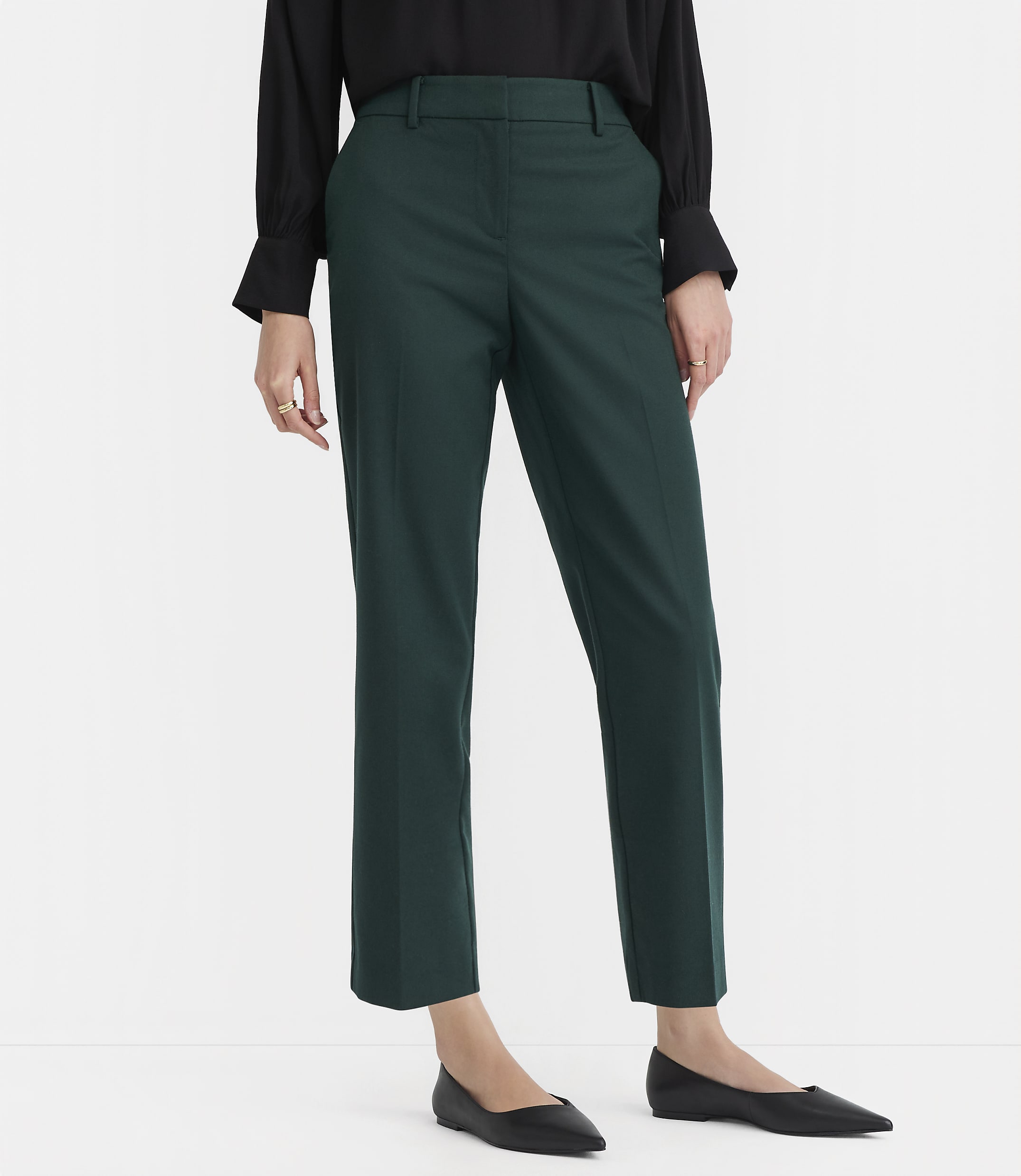 A person in a black shirt and green pants stands on a white background.