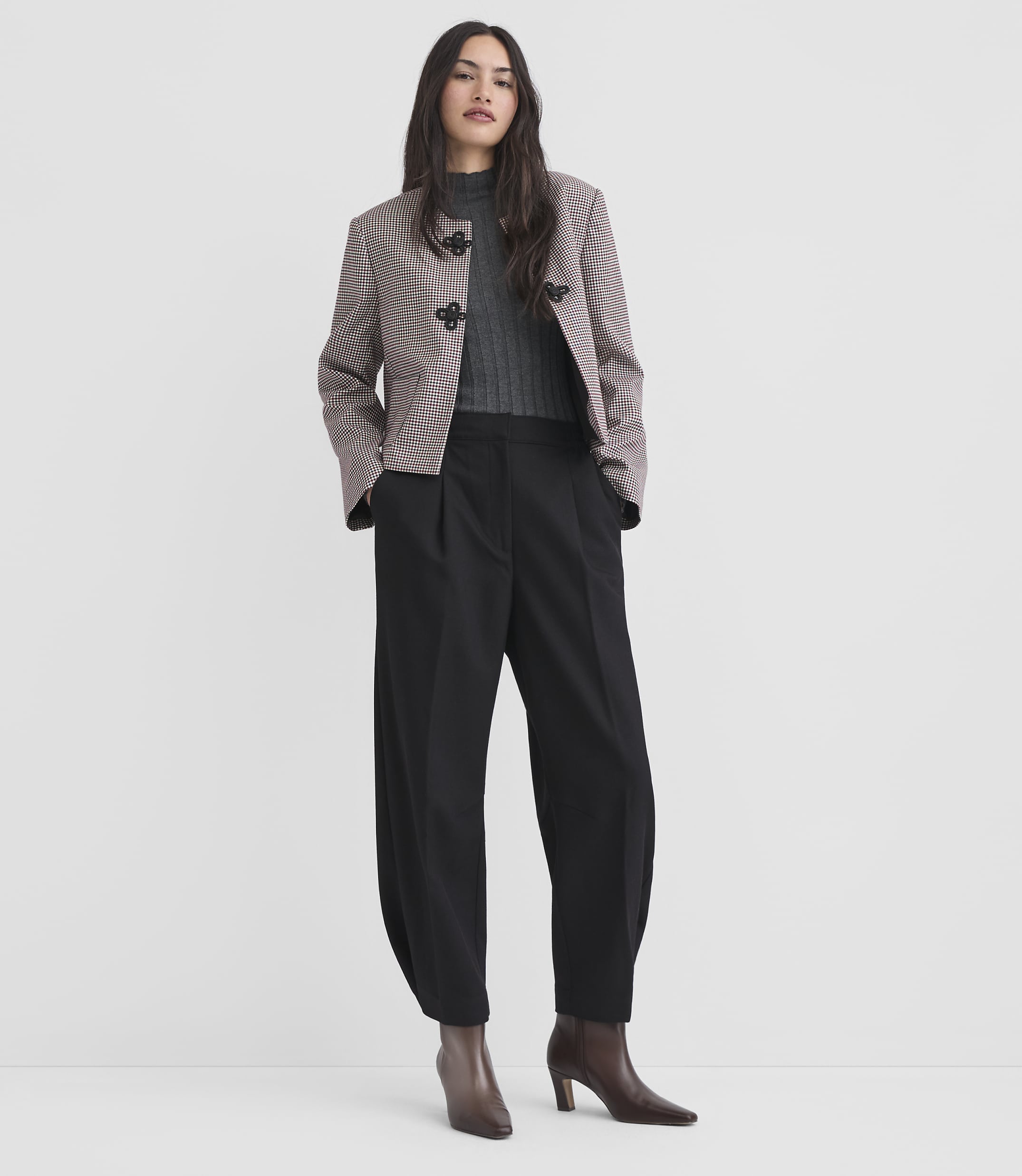 A woman in a patterned jacket and black pants stands against a plain white background.