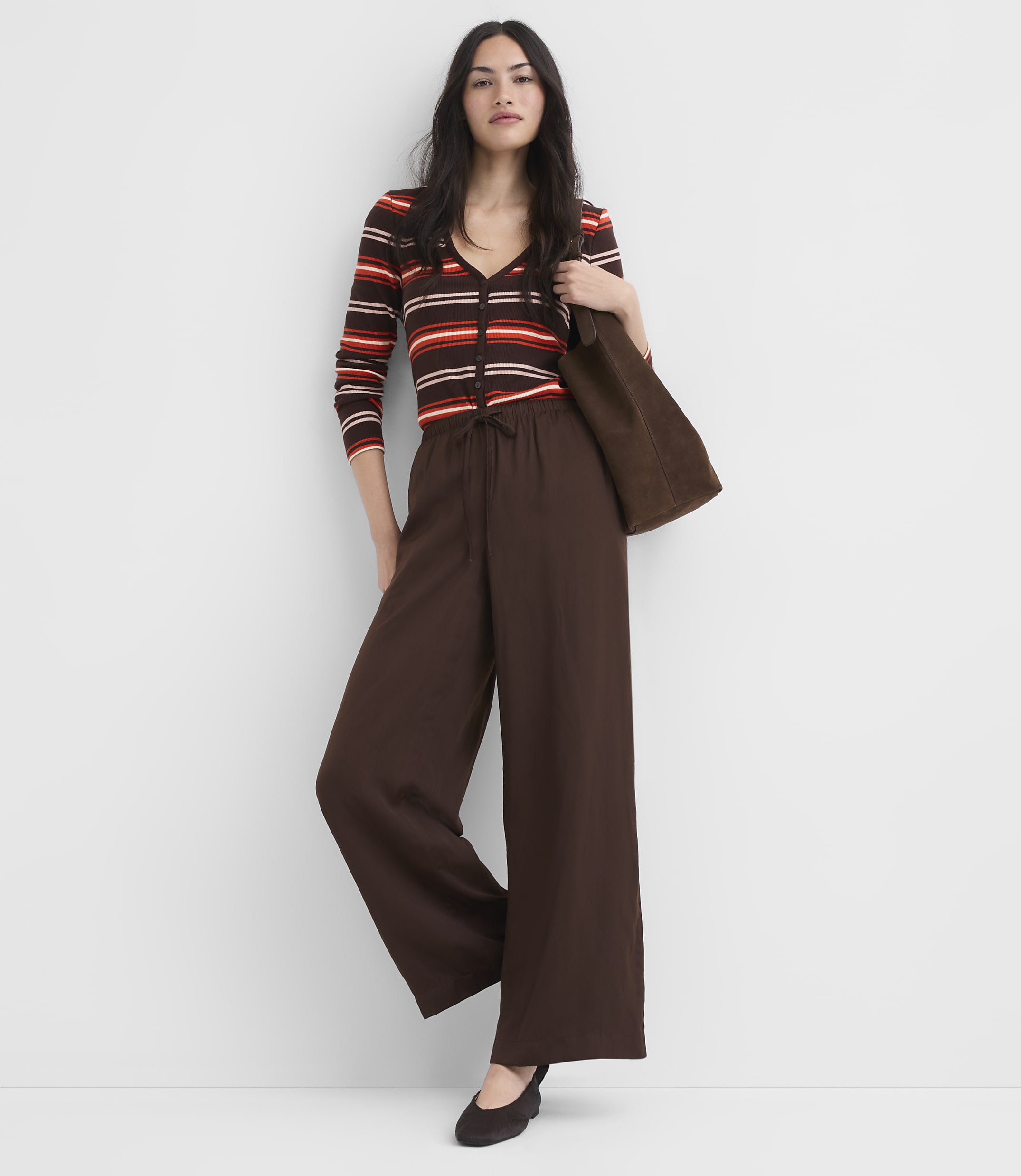 A woman in a striped top and wide-leg pants stands against a plain white background.