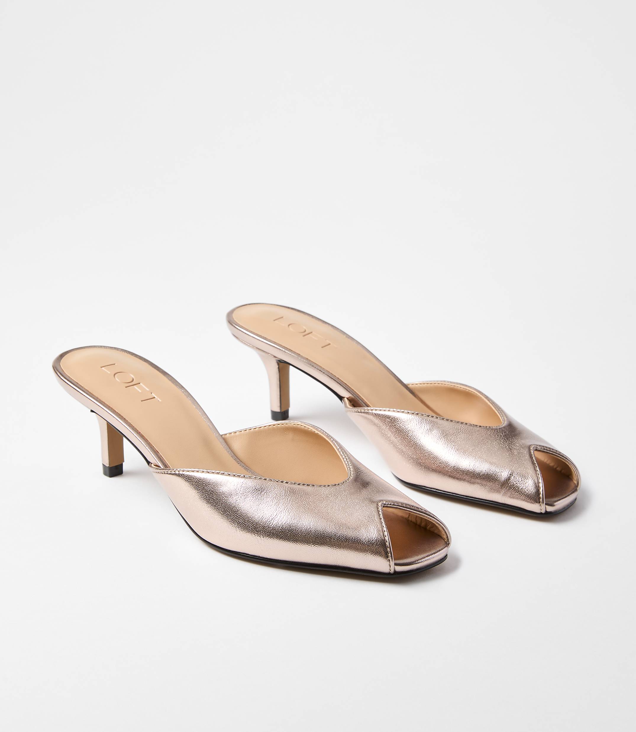 A pair of rose gold peep-toe mules with kitten heels rests on a plain white background.