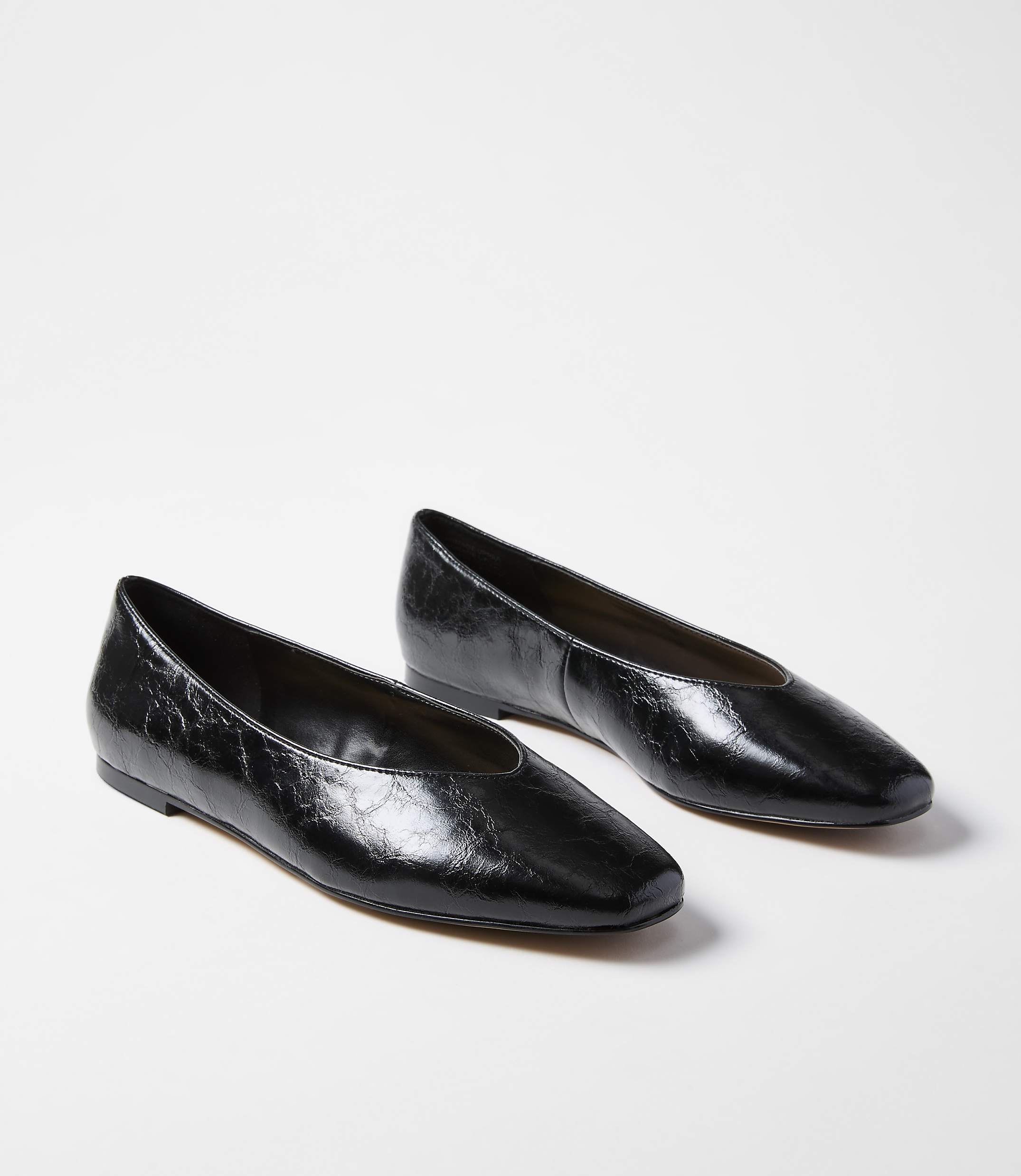 A pair of glossy black square-toe ballet flats rests on a plain white background.