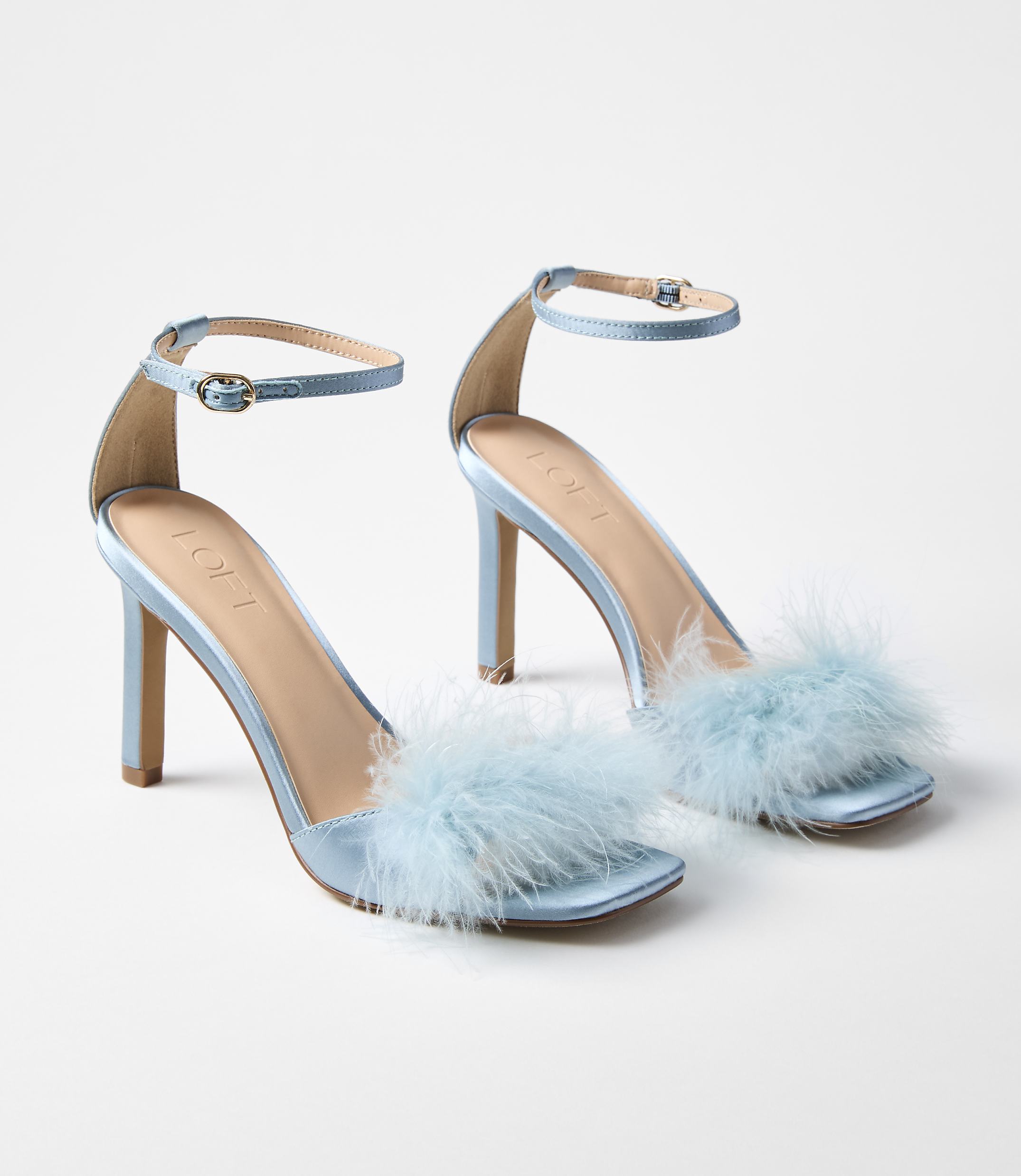A pair of light blue satin heeled sandals with fluffy trim are displayed against a plain white background.