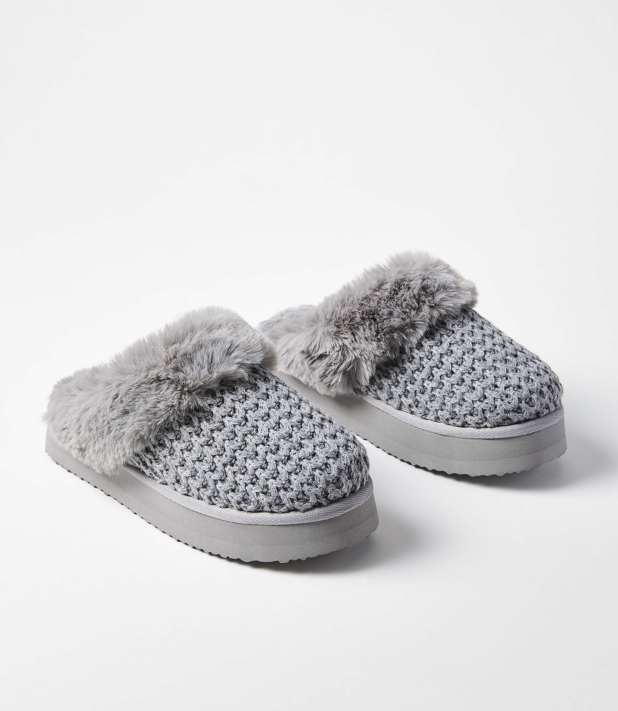 A pair of gray knitted slippers with faux fur trim rests on a white background.