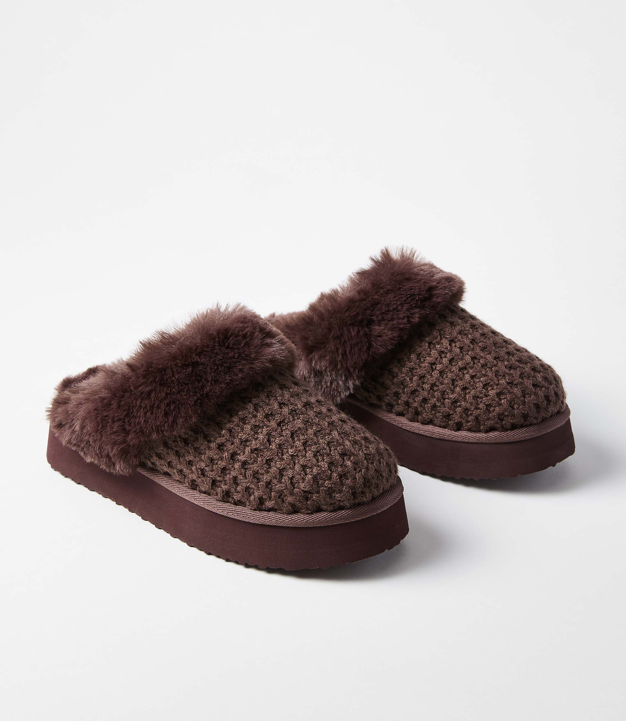 A pair of brown knitted slippers with fluffy trim rests on a white background.