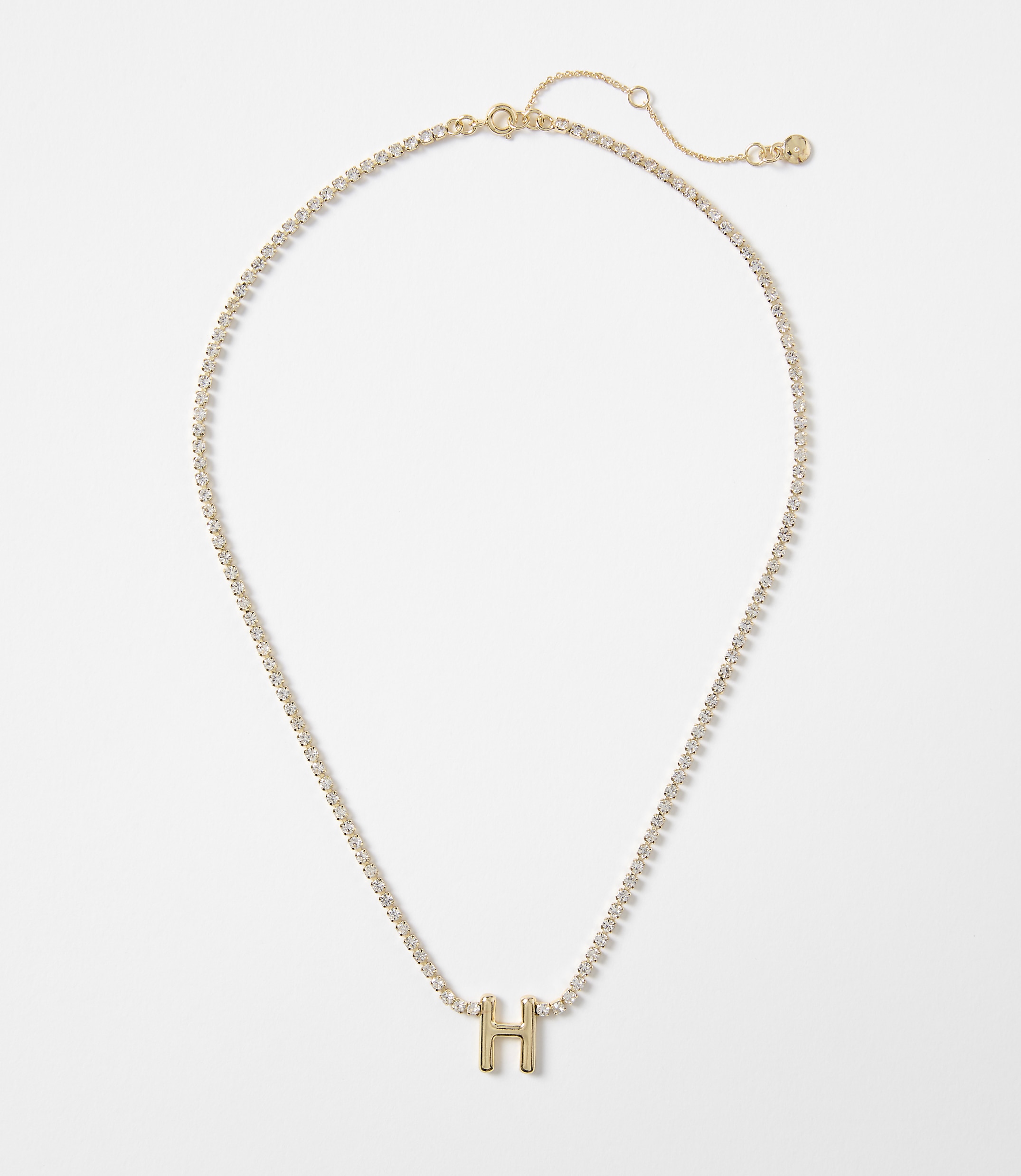 A gold necklace with a sparkling chain and a gold letter "H" pendant rests against a plain white background.