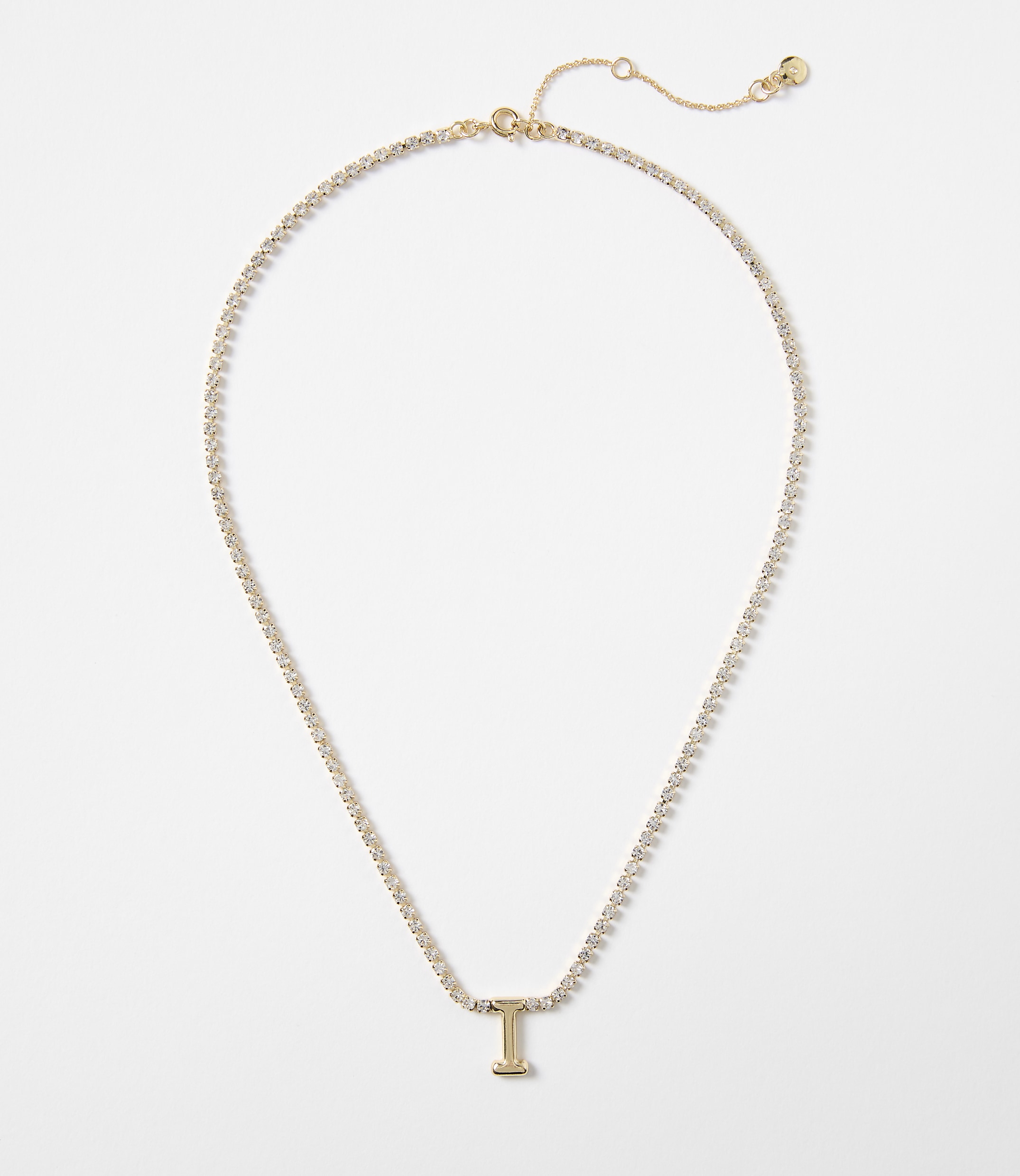 A delicate gold chain necklace with a sparkling "I" pendant rests on a plain white background.