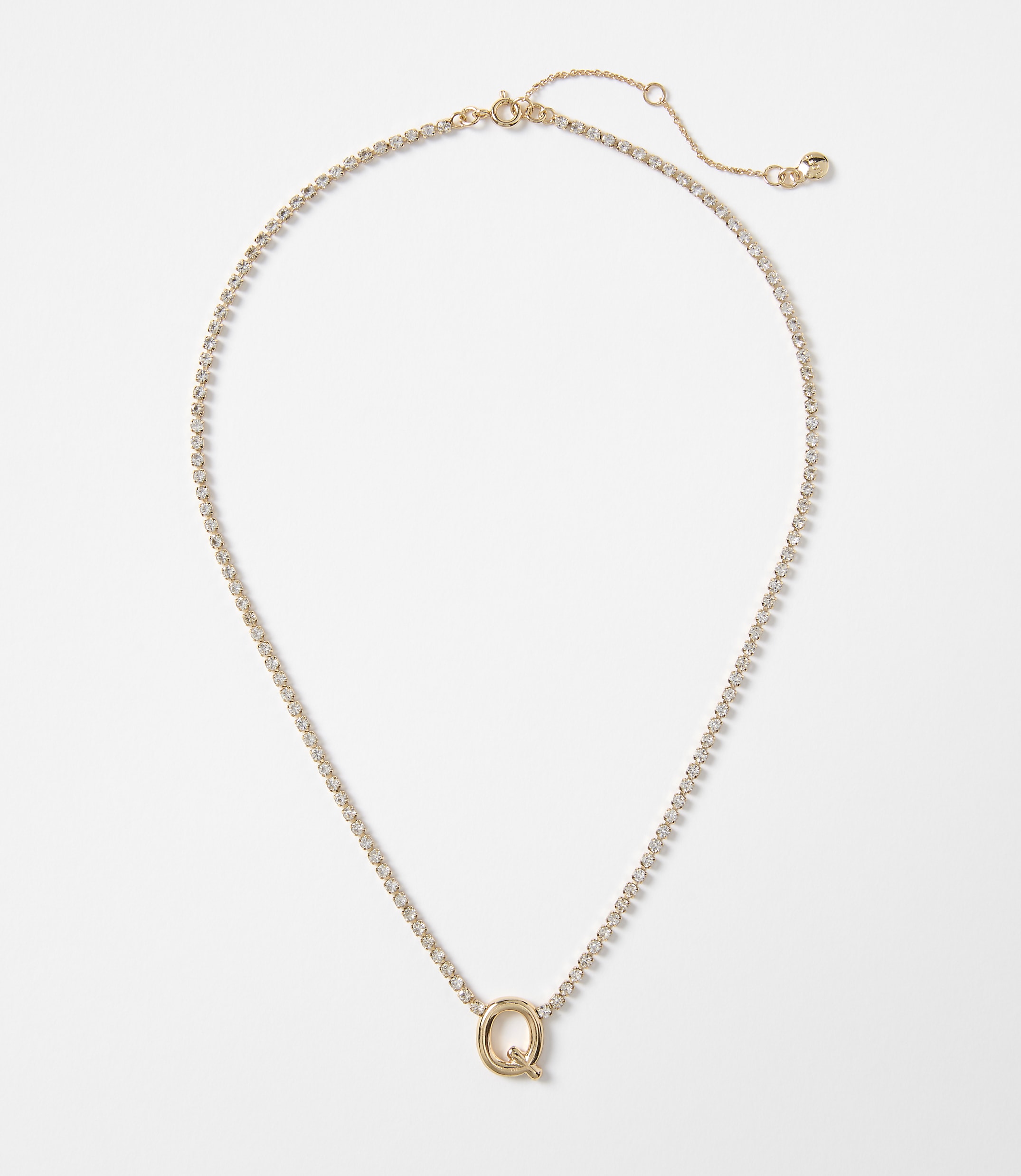 A delicate gold necklace with a sparkling "Q" pendant rests on a plain white background.