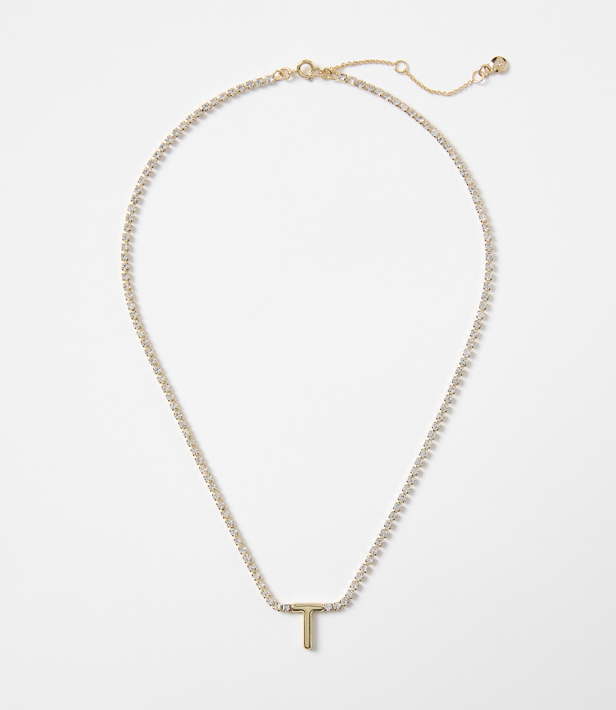 A delicate gold chain with a sparkling "T" pendant rests against a plain white background.