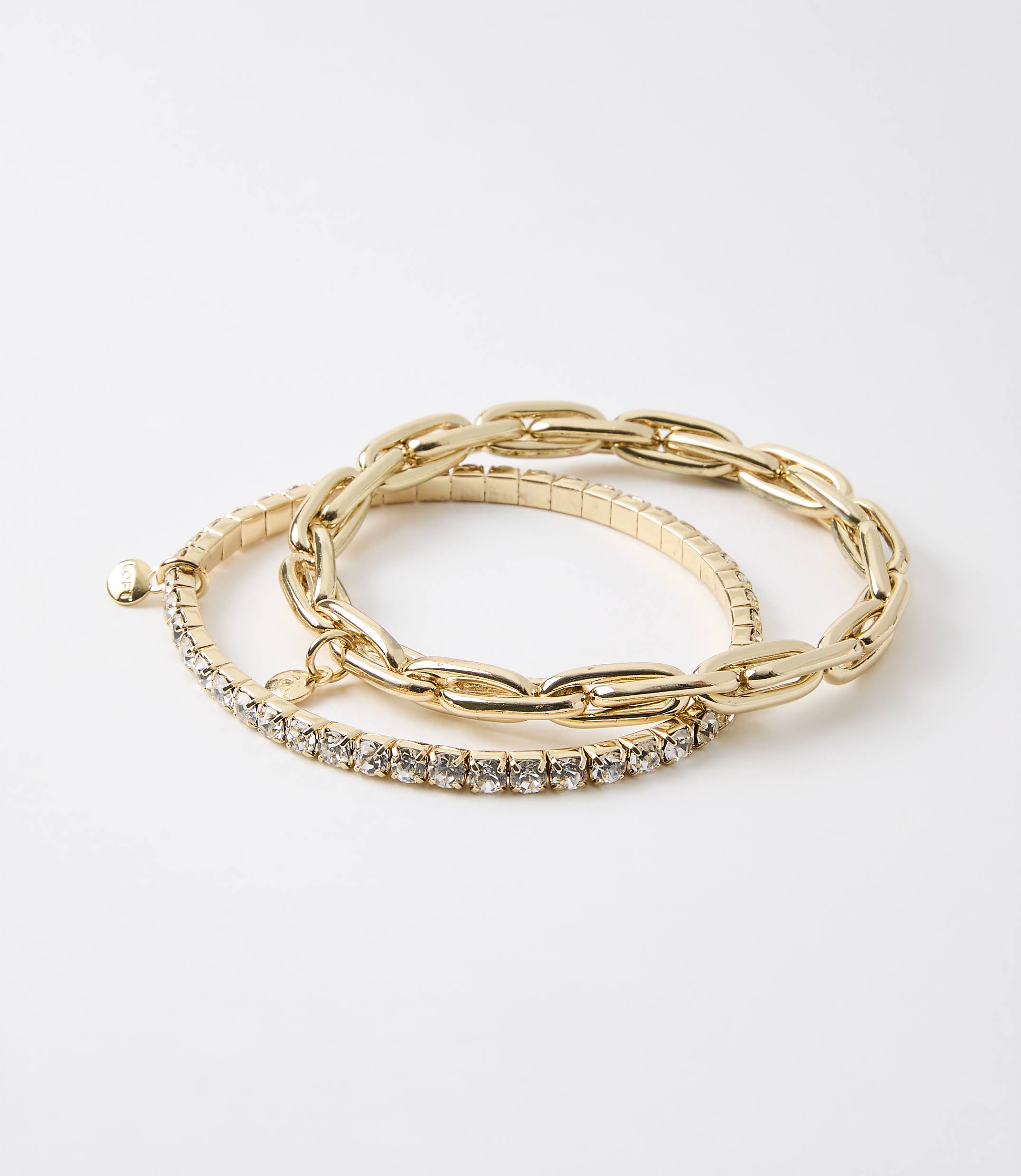 Two gold bracelets, one with a chunky chain design and the other with a band of small rhinestones, rest on a plain white background.