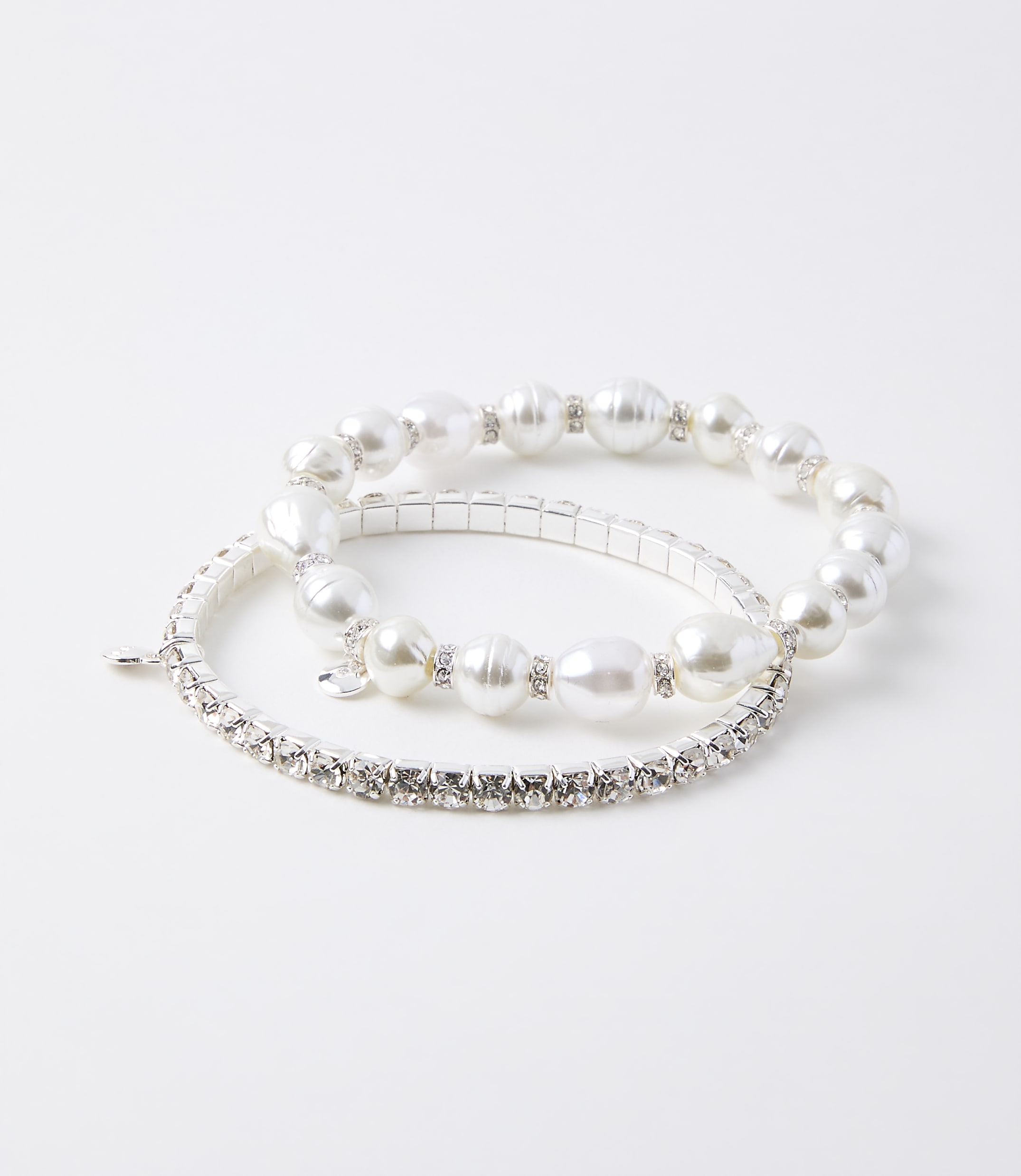 Two bracelets, one with pearls and rhinestones and another with only rhinestones, rest on a plain white background.