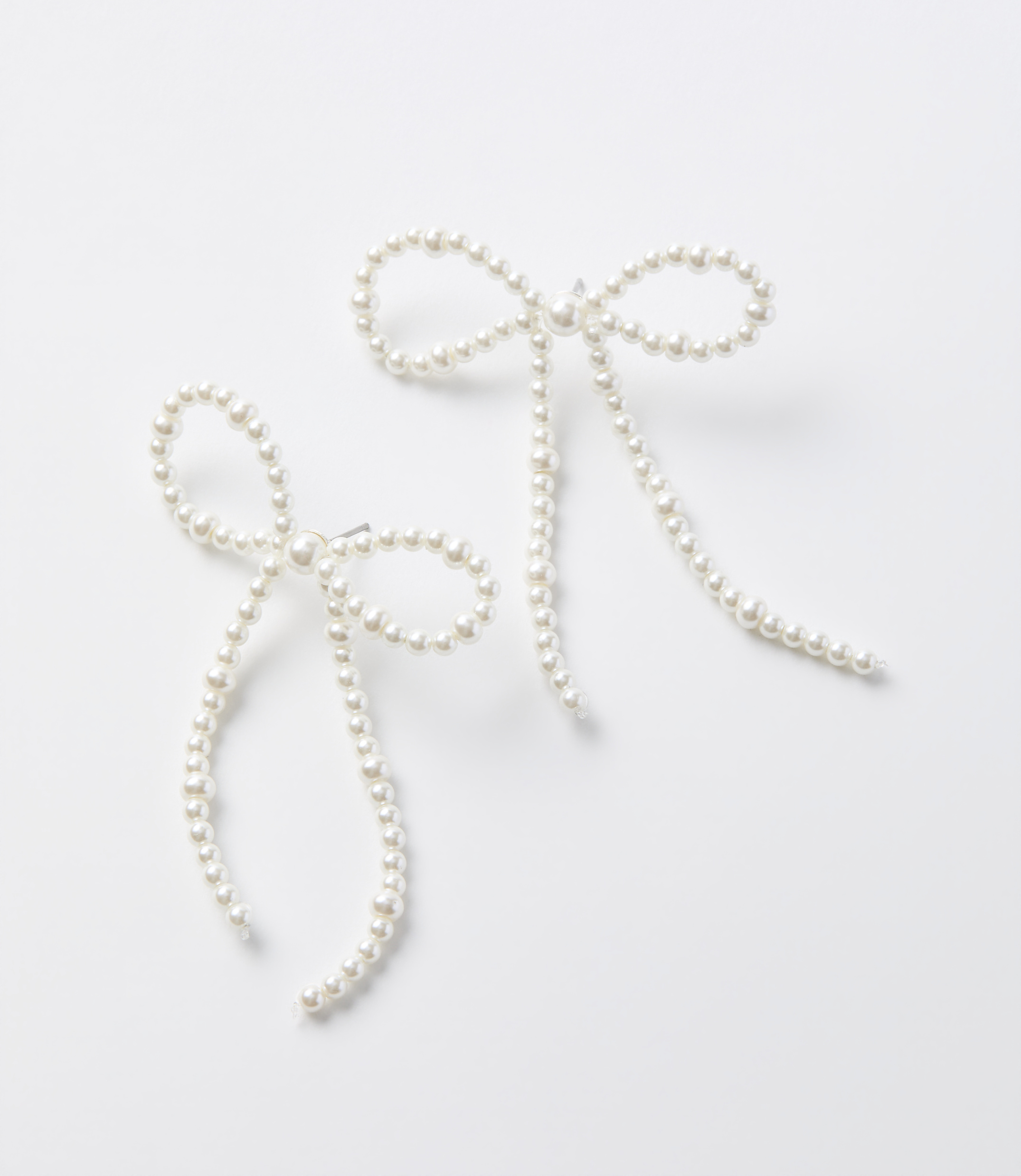 Two delicate pearl bow earrings with dangling strands are arranged on a plain white background.