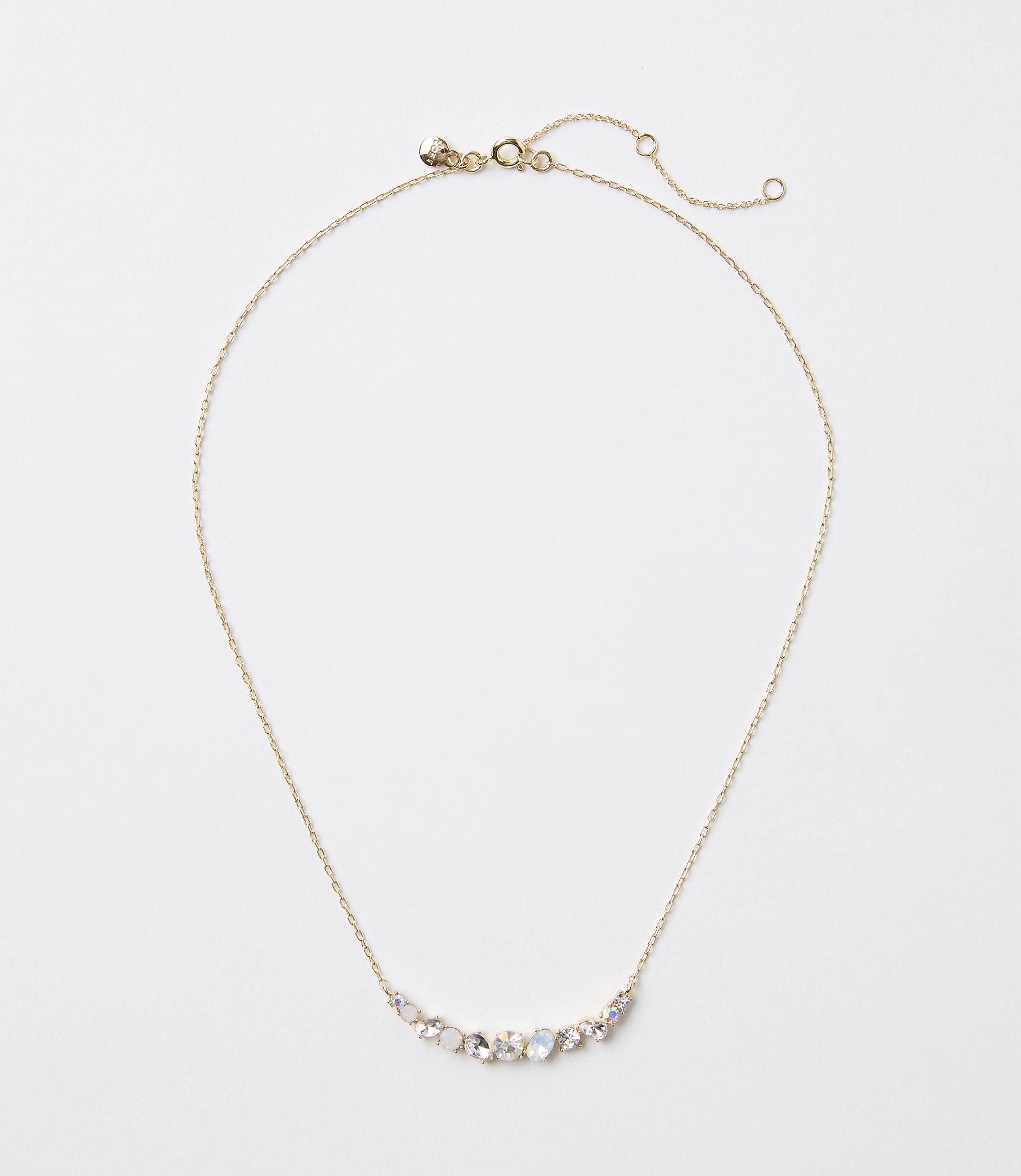 A delicate gold necklace with a curved arrangement of small, iridescent stones rests on a plain white background.