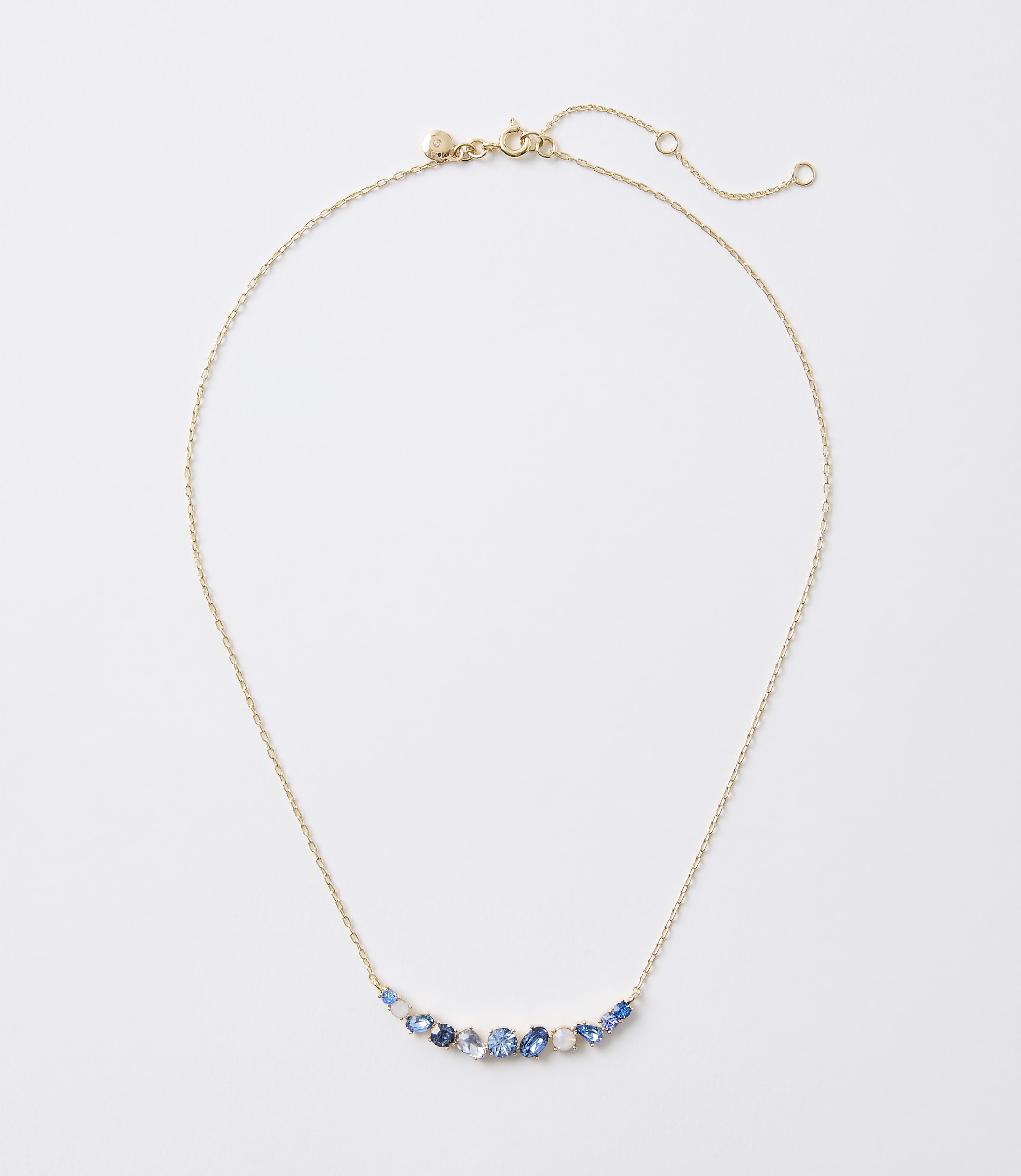 A delicate gold necklace with a curved arrangement of blue and white gemstones rests on a plain white background.
