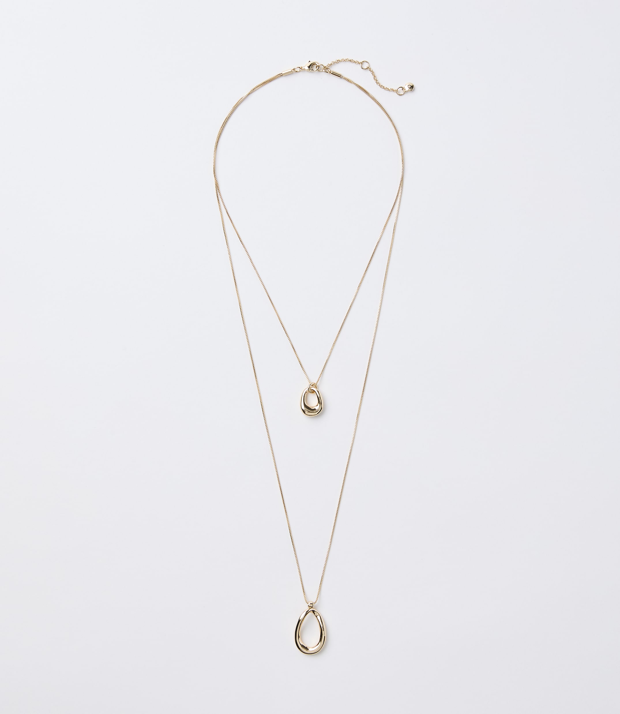 A delicate gold layered necklace with two abstract pendant shapes hangs against a plain white background.