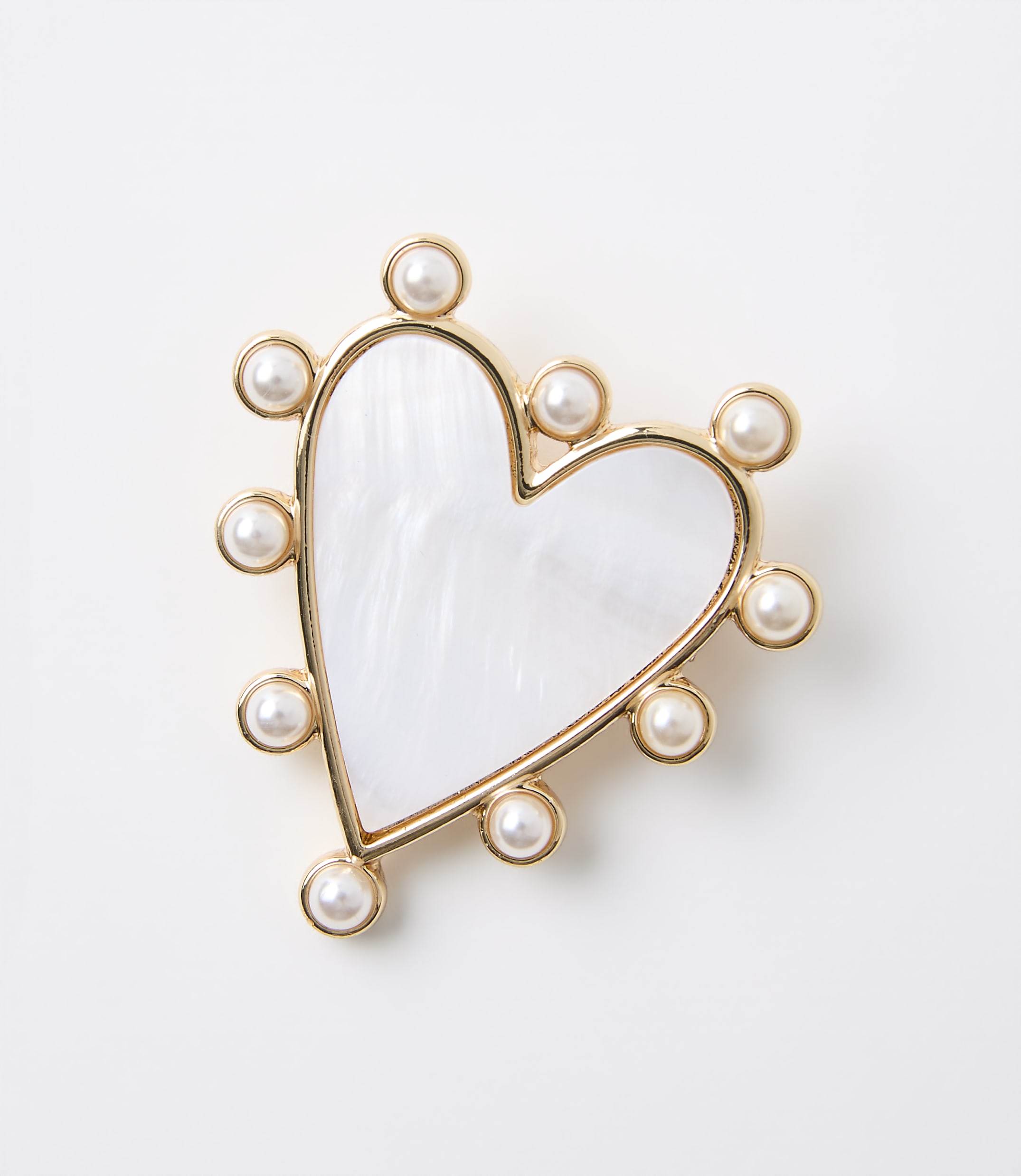 A white, heart-shaped brooch with a mother-of-pearl inlay and a border of small pearls sits against a plain white background.