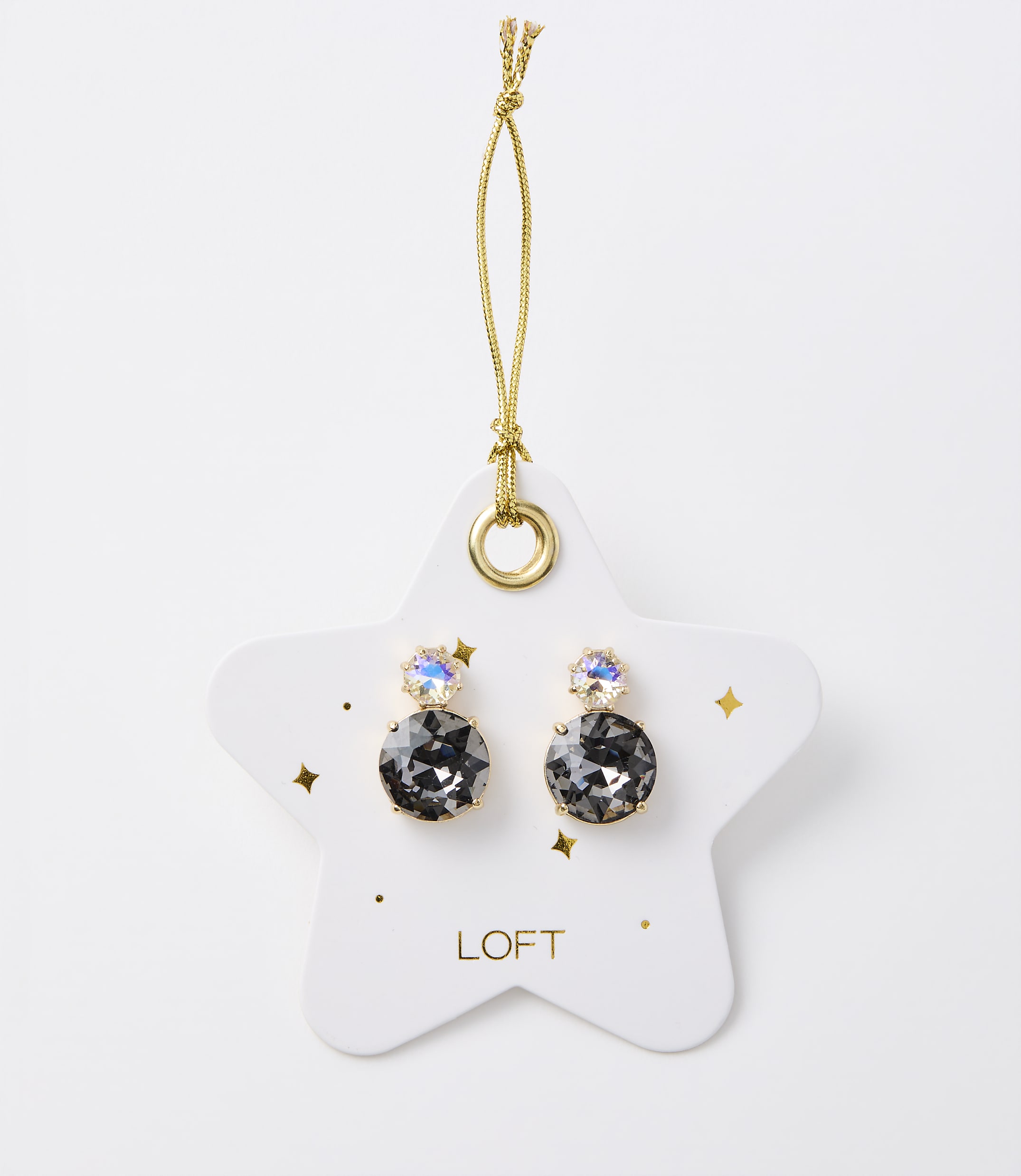 A pair of dark gray stud earrings with iridescent accents hang from a gold string on a white star-shaped card with gold speckles and the "LOFT" logo, set against a plain white background.