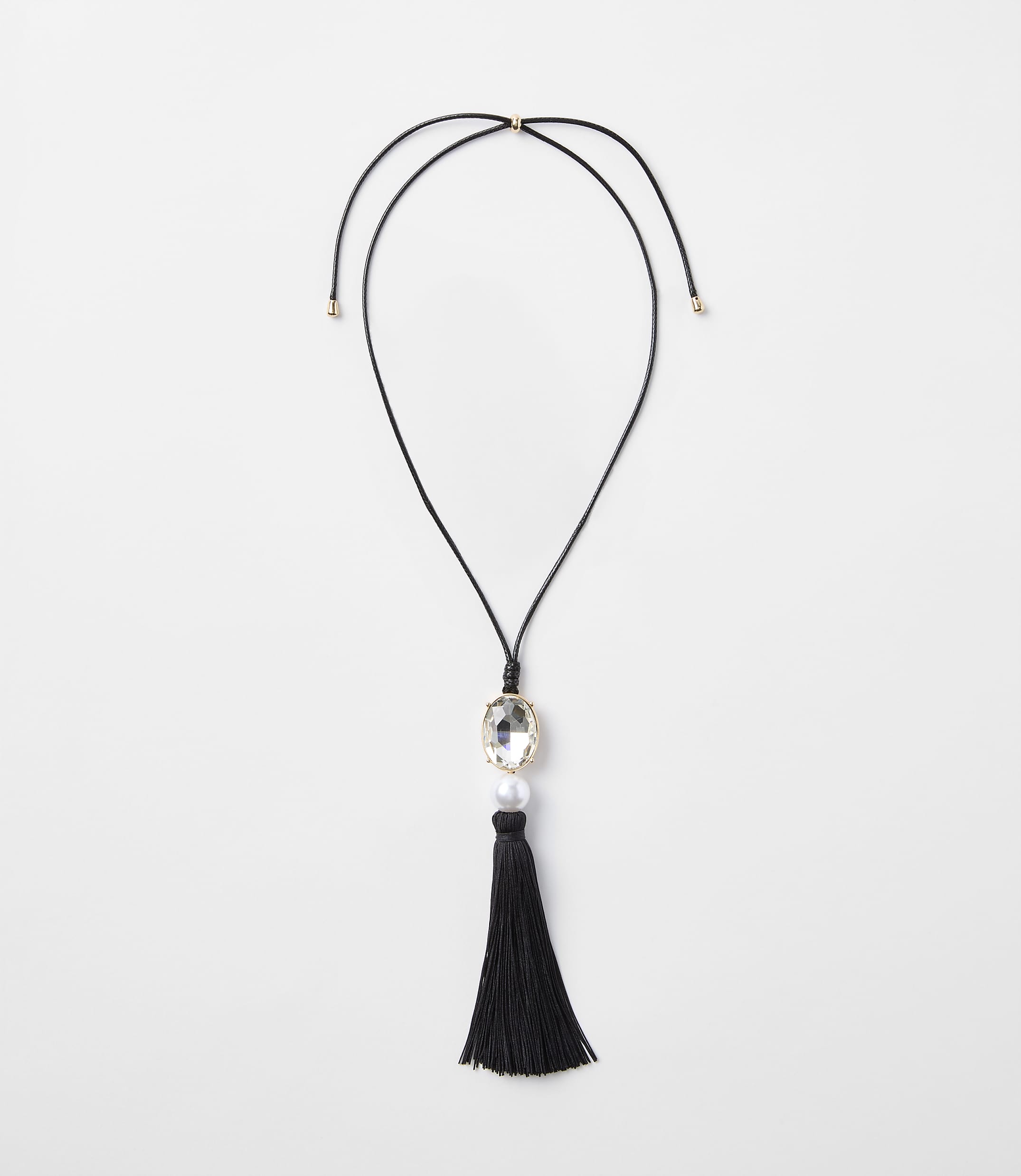 A black tassel necklace with a clear gem and pearl hangs against a plain white background.