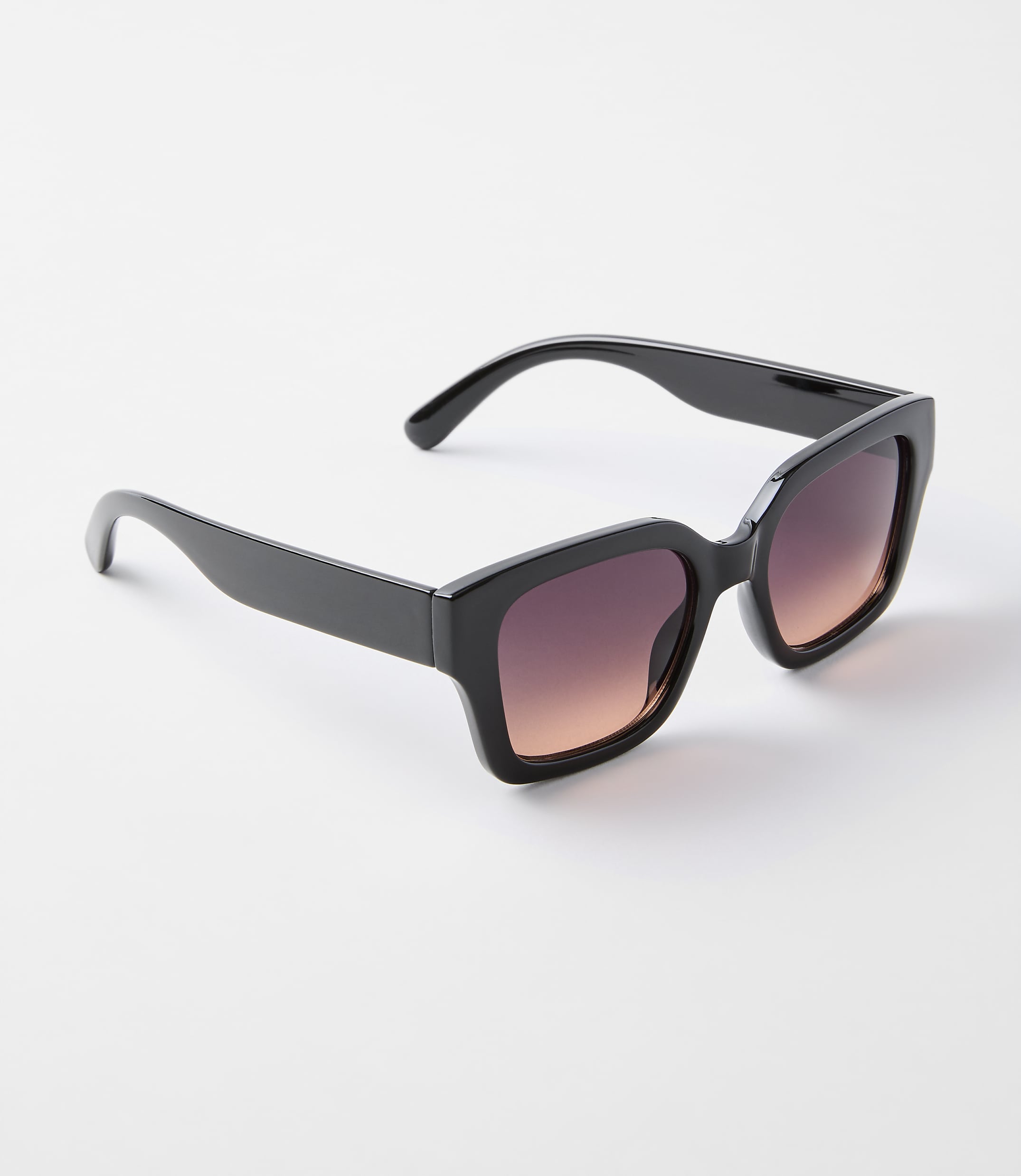 A pair of black, oversized sunglasses with gradient lenses rests on a plain white background.