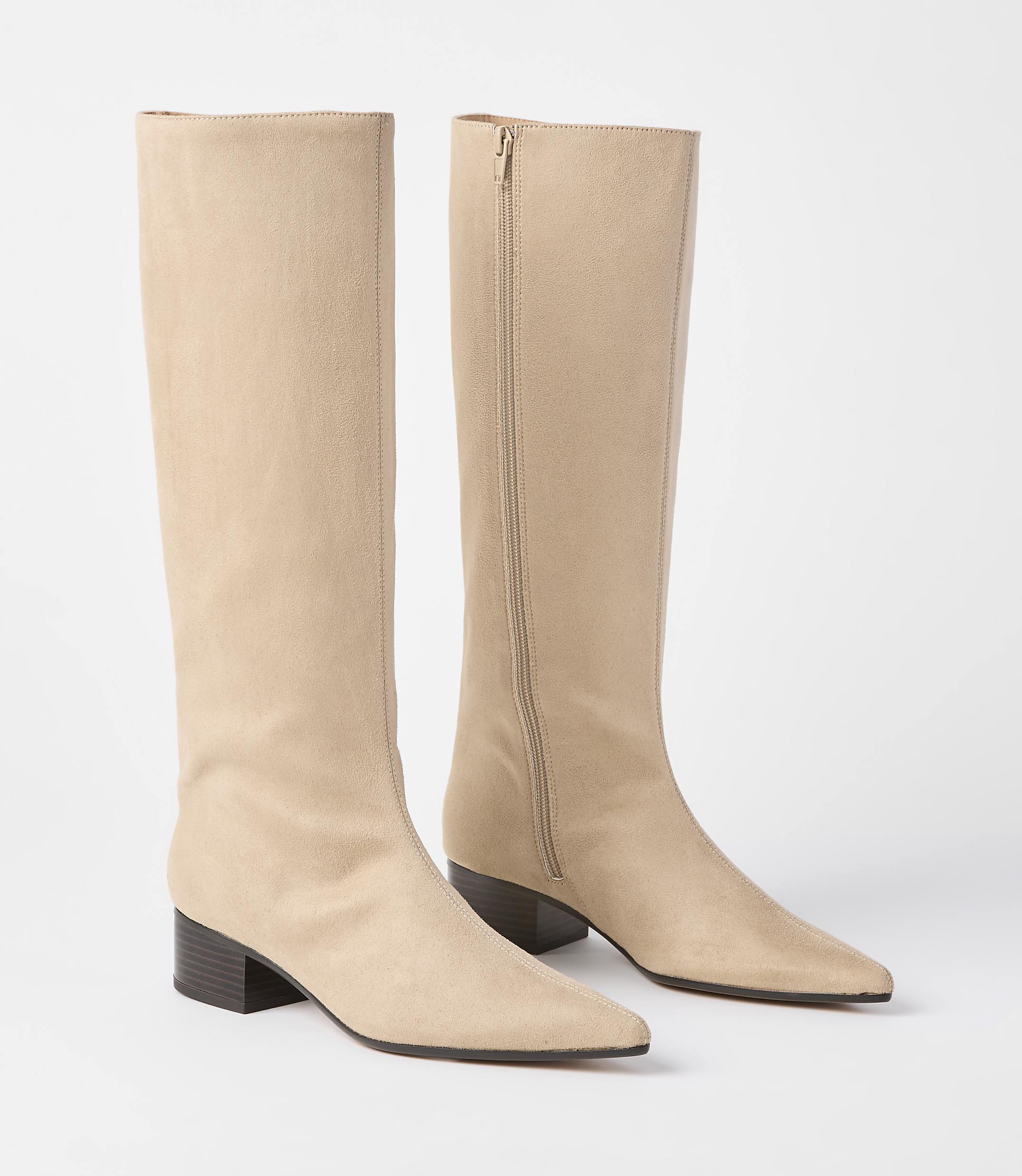A pair of beige suede knee-high boots with pointed toes and block heels stand on a plain white background.