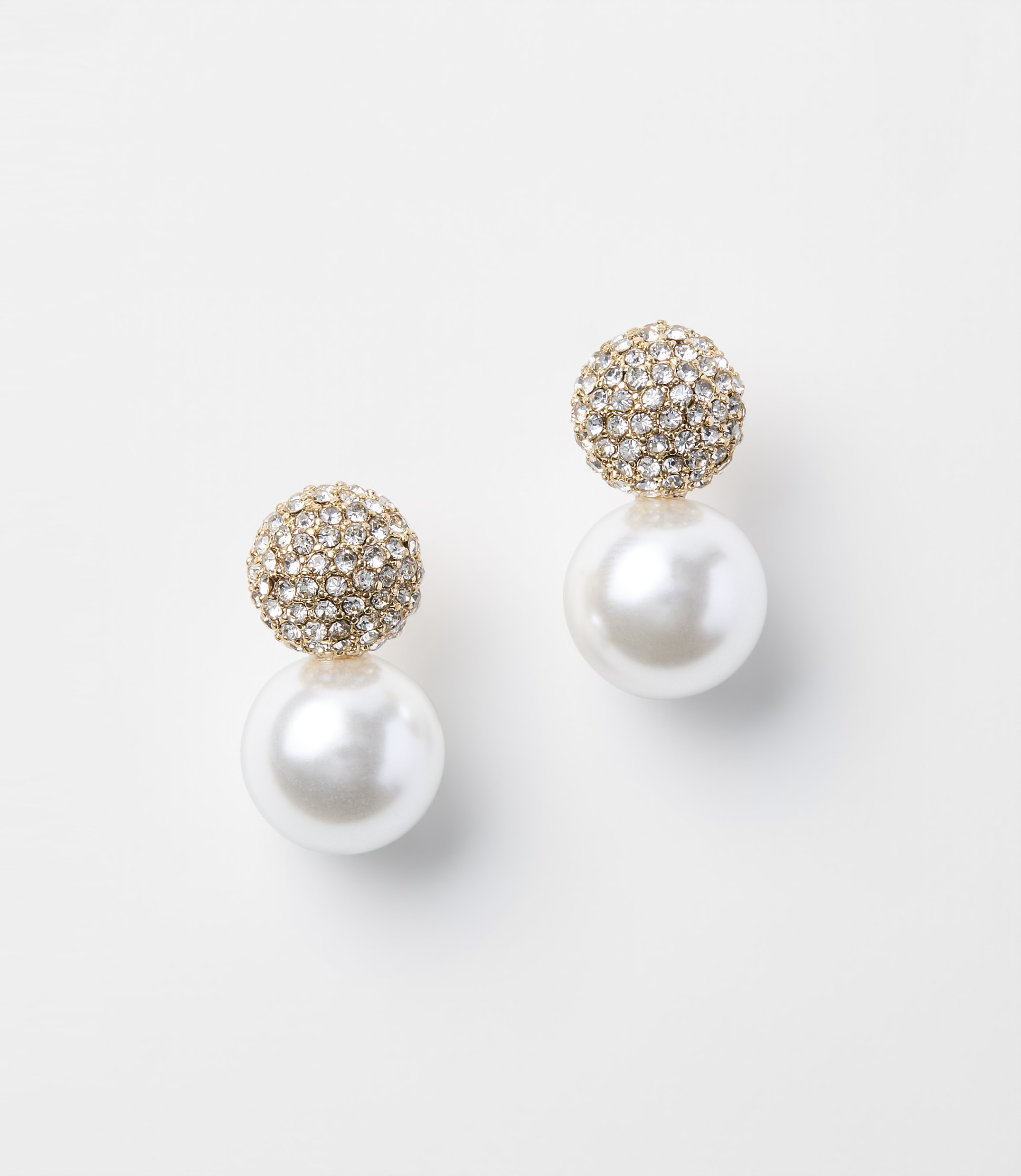 A pair of pearl drop earrings with crystal-encrusted tops rest on a plain white background.