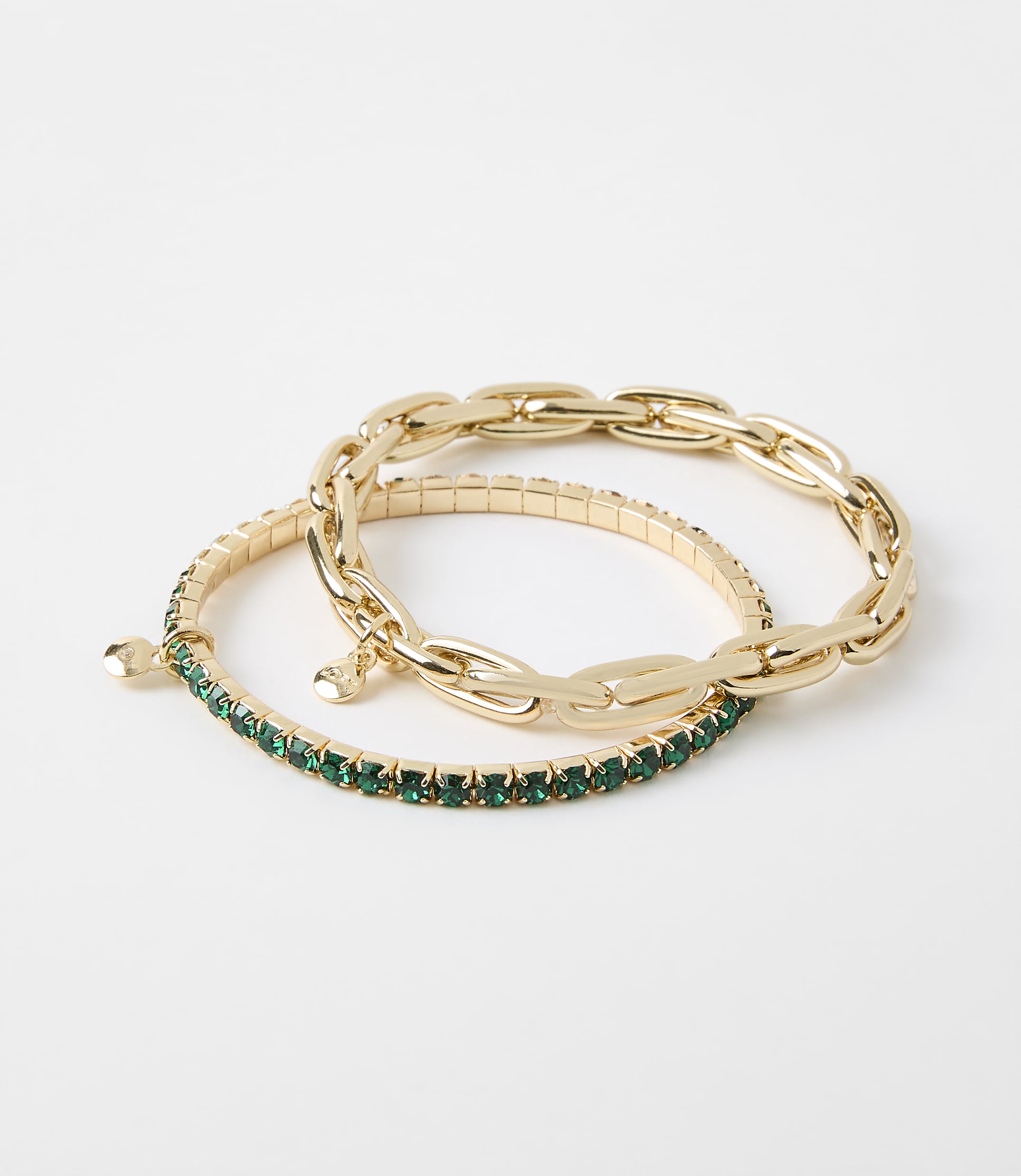Two gold bracelets, one with a chunky chain design and the other adorned with green gemstones, rest on a plain white background.