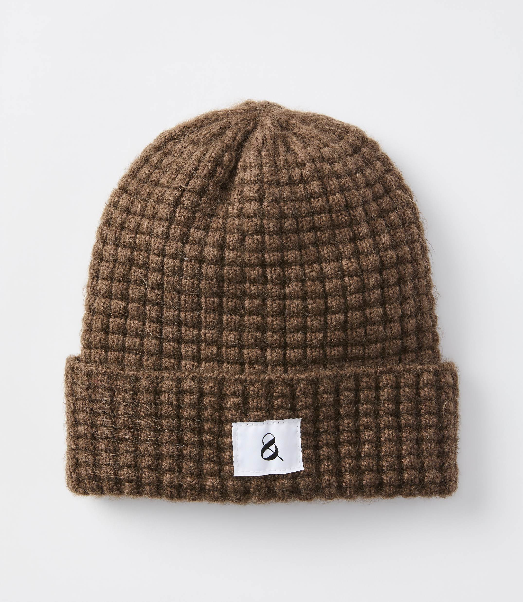 A brown waffle-knit beanie with a white tag featuring a black ampersand sits against a plain white background.
