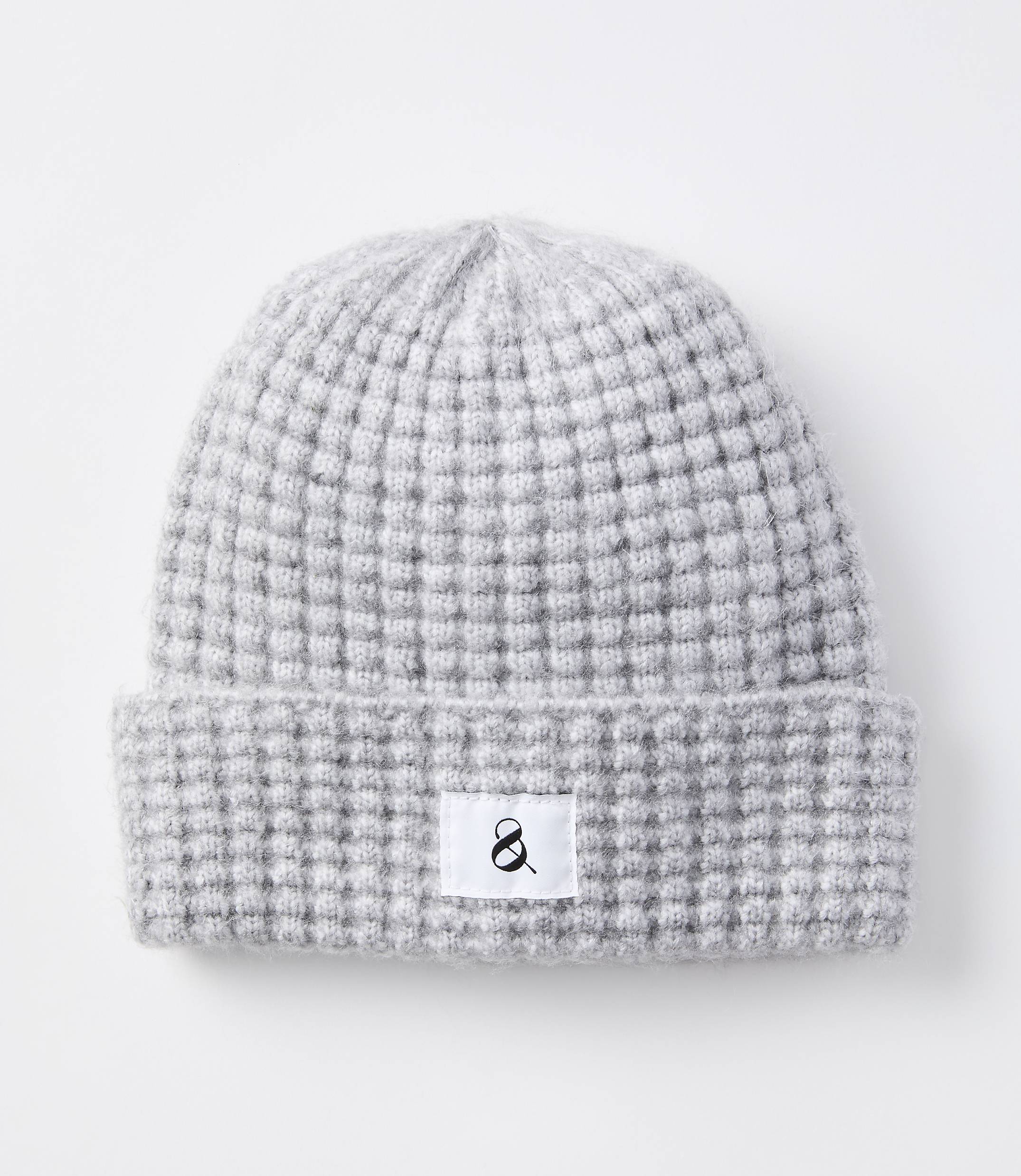 A light gray knitted beanie with a waffle knit pattern and a white tag with a black ampersand sits on a plain white background.