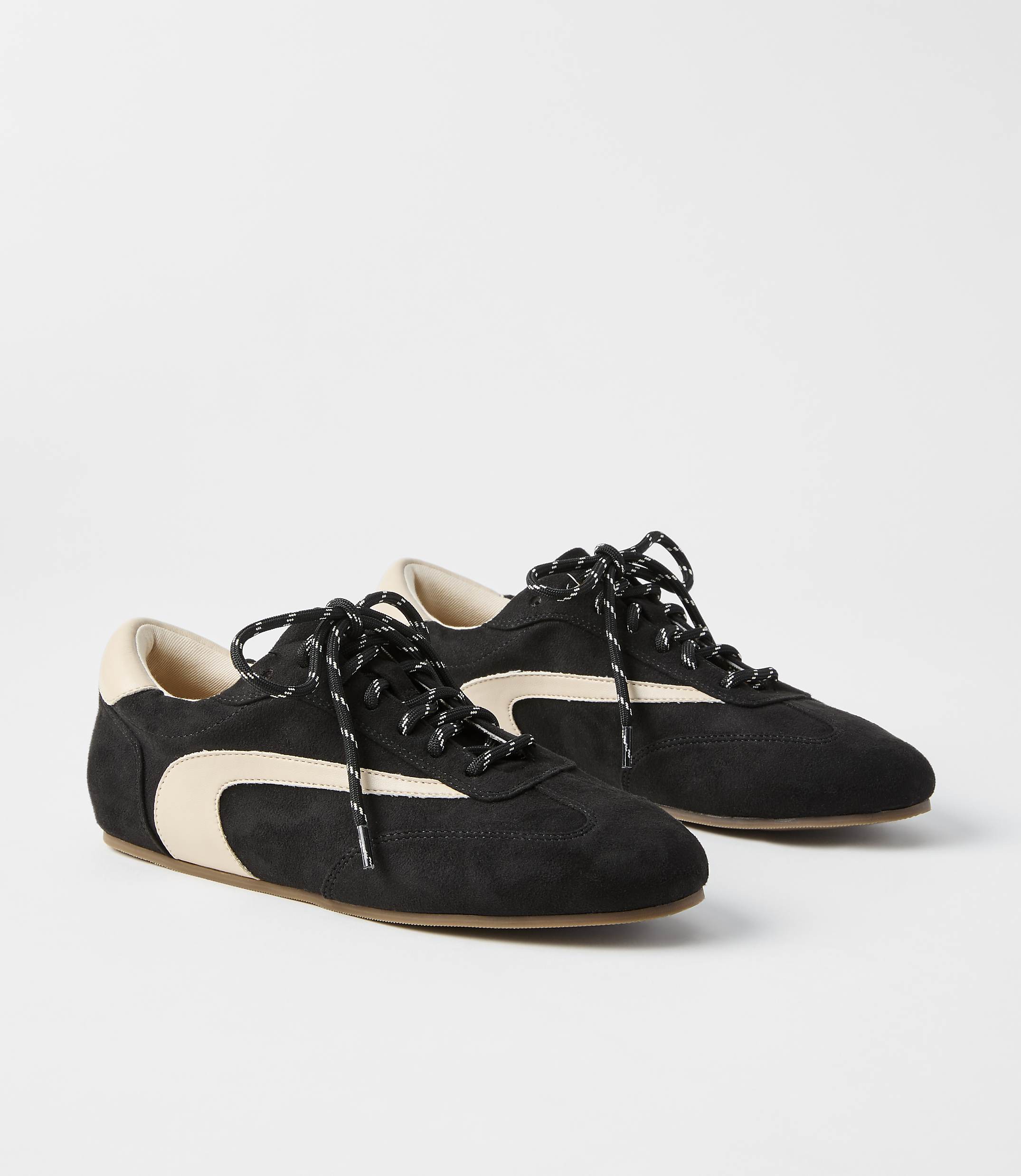 A pair of black suede sneakers with cream accents and black laces rests on a plain white background.