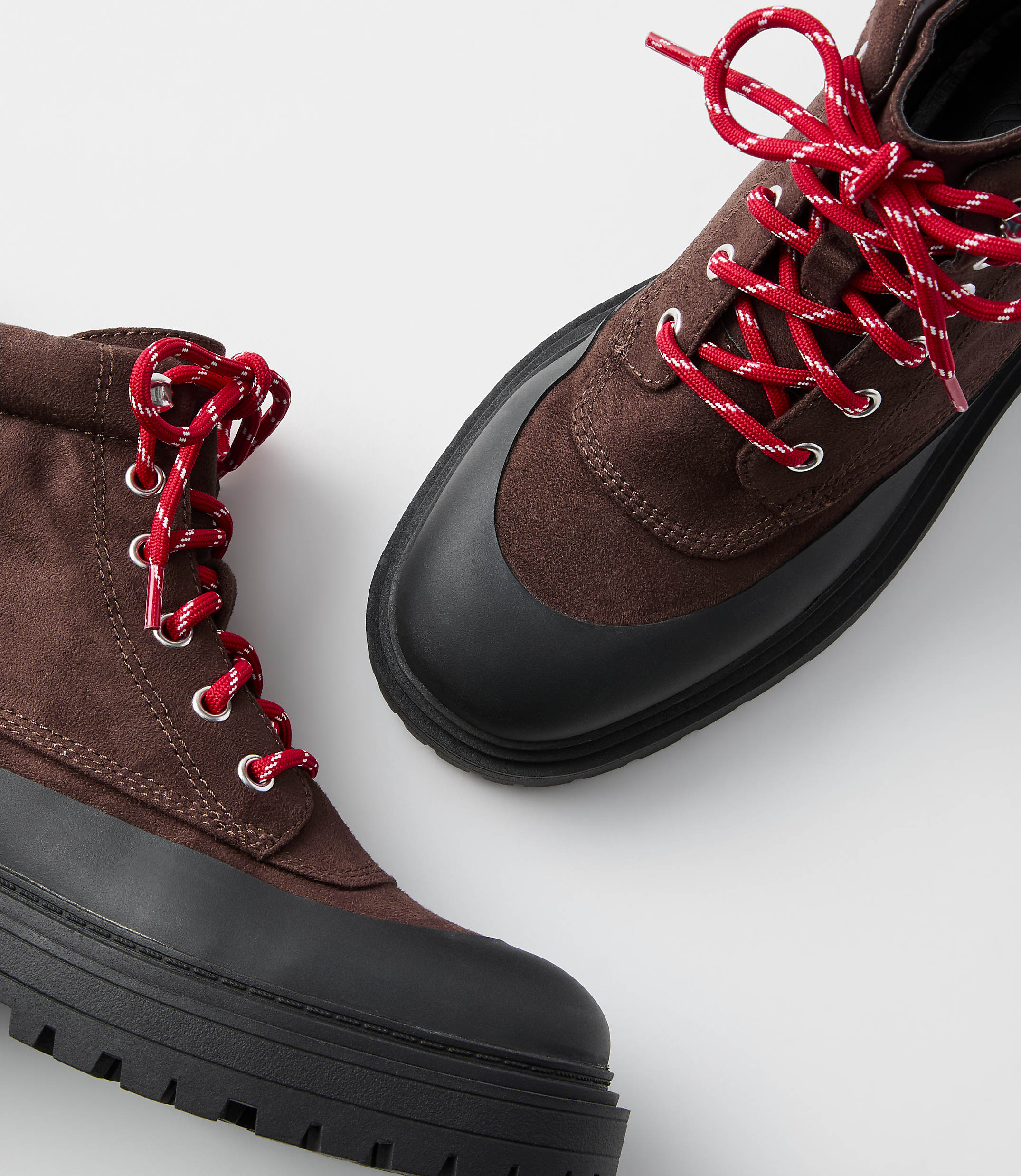A pair of brown lace-up boots with thick black soles and red laces are displayed against a plain white background.