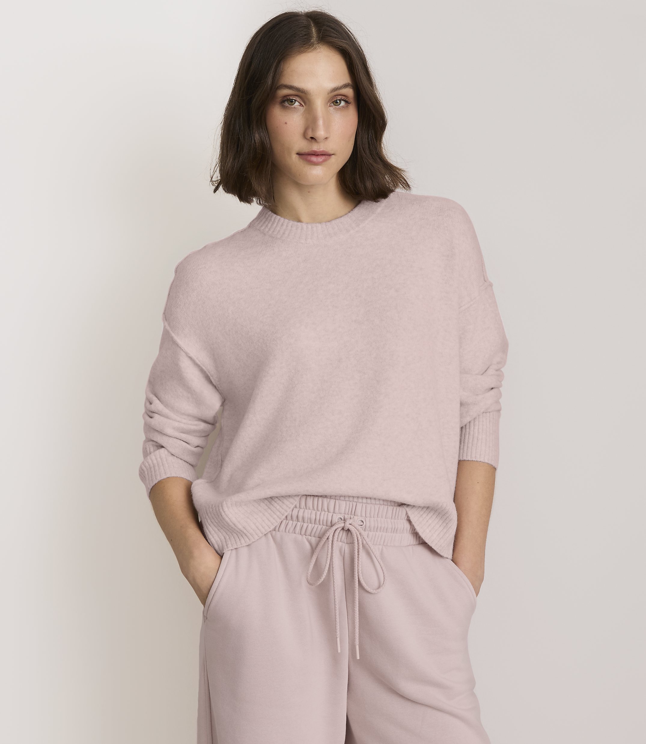 A woman in a pink sweater and matching pants stands against a plain, light background.