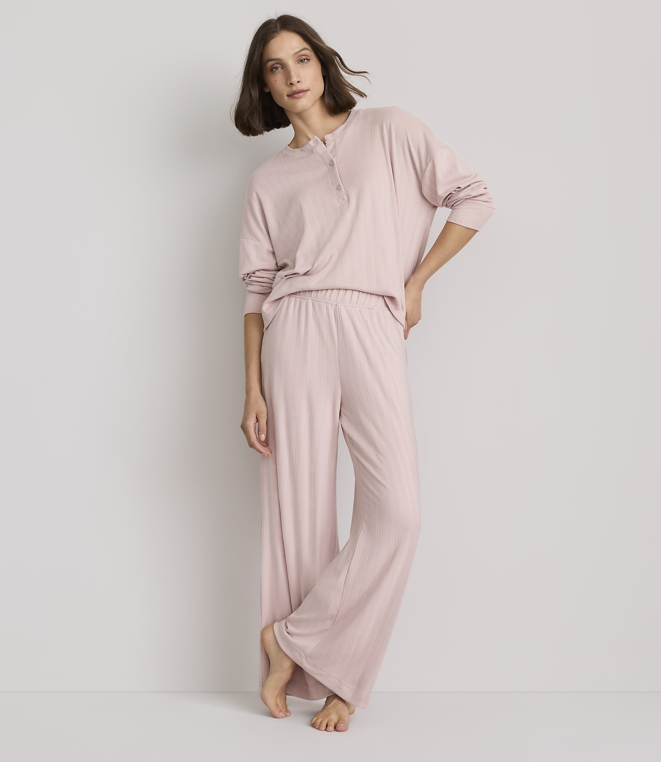 A woman in pink pajamas stands against a plain, light gray background.