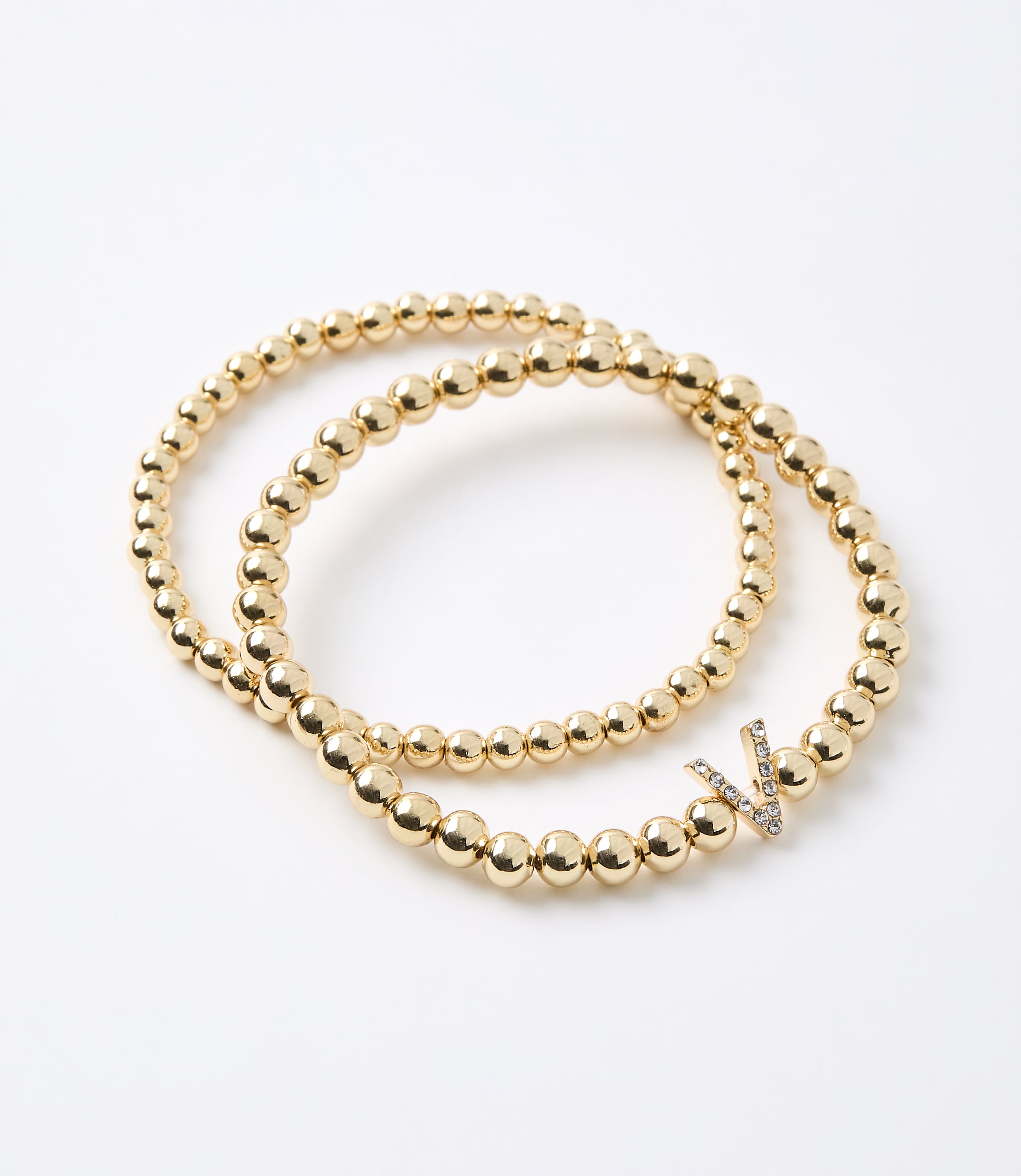 Two gold beaded bracelets, one with a diamond-encrusted "V" charm, rest on a plain white background.