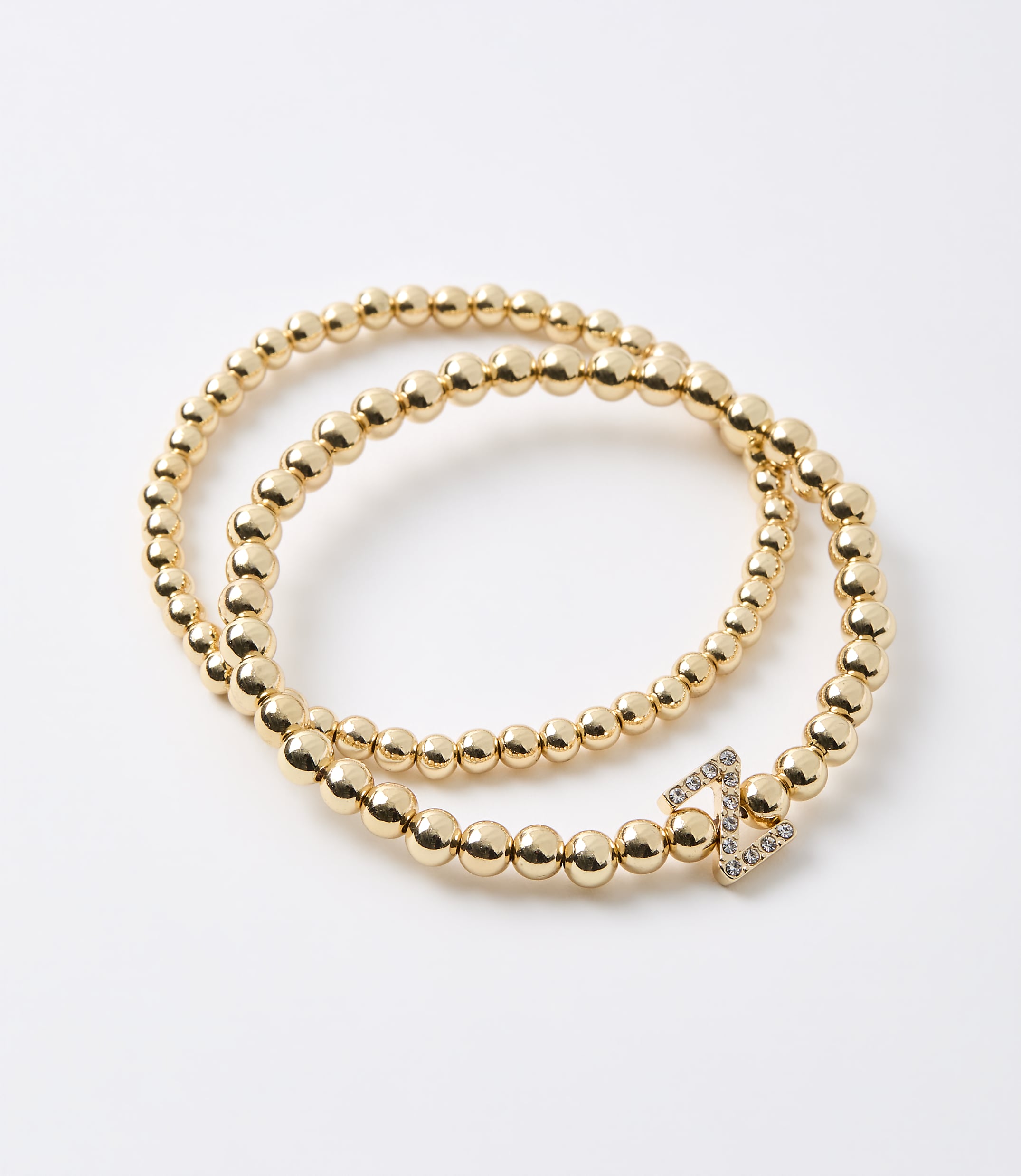 A gold beaded bracelet with a diamond-encrusted clasp is coiled on a plain white background.