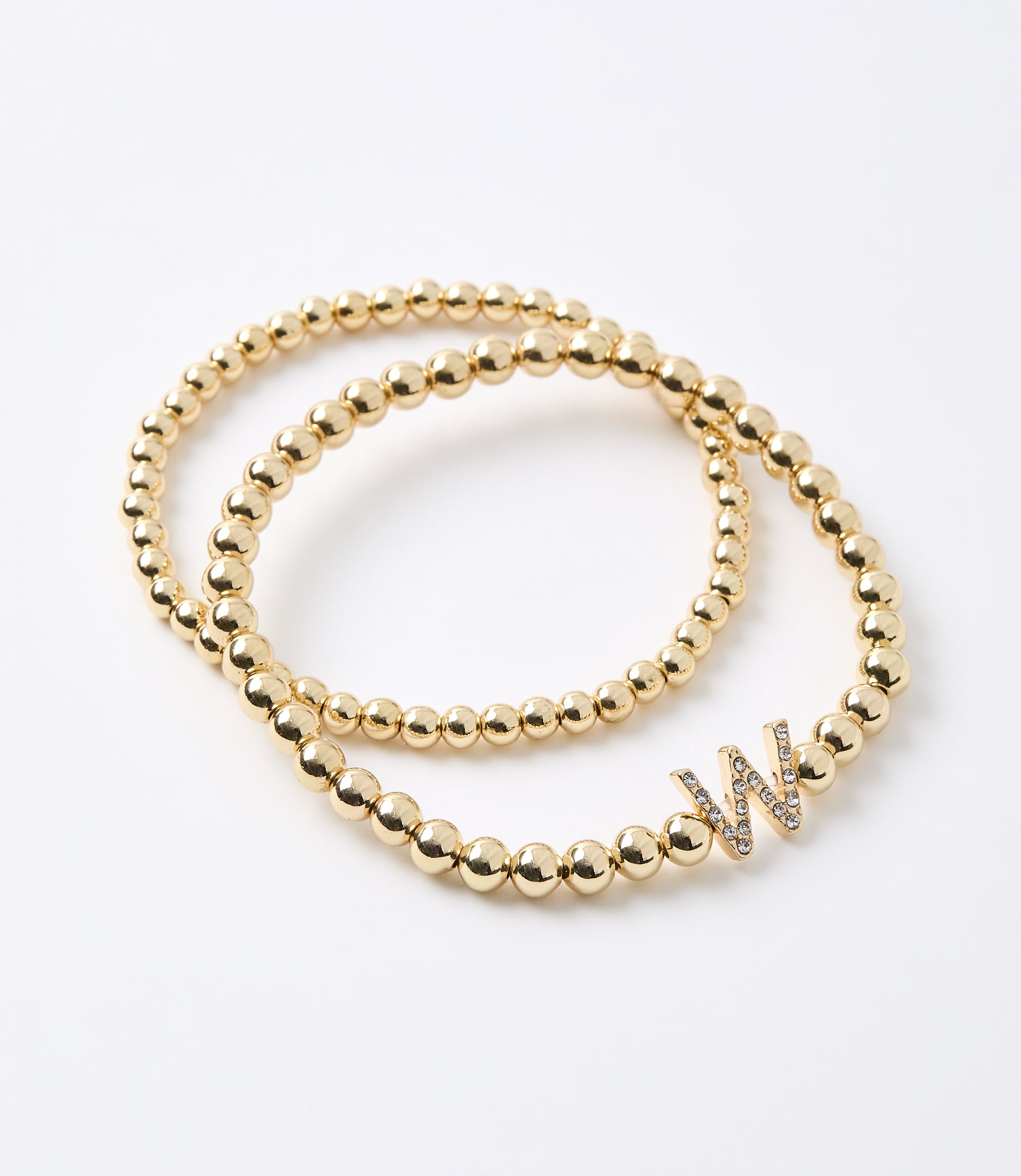 Two gold beaded bracelets, one with a diamond-encrusted "W" charm, rest on a plain white background.