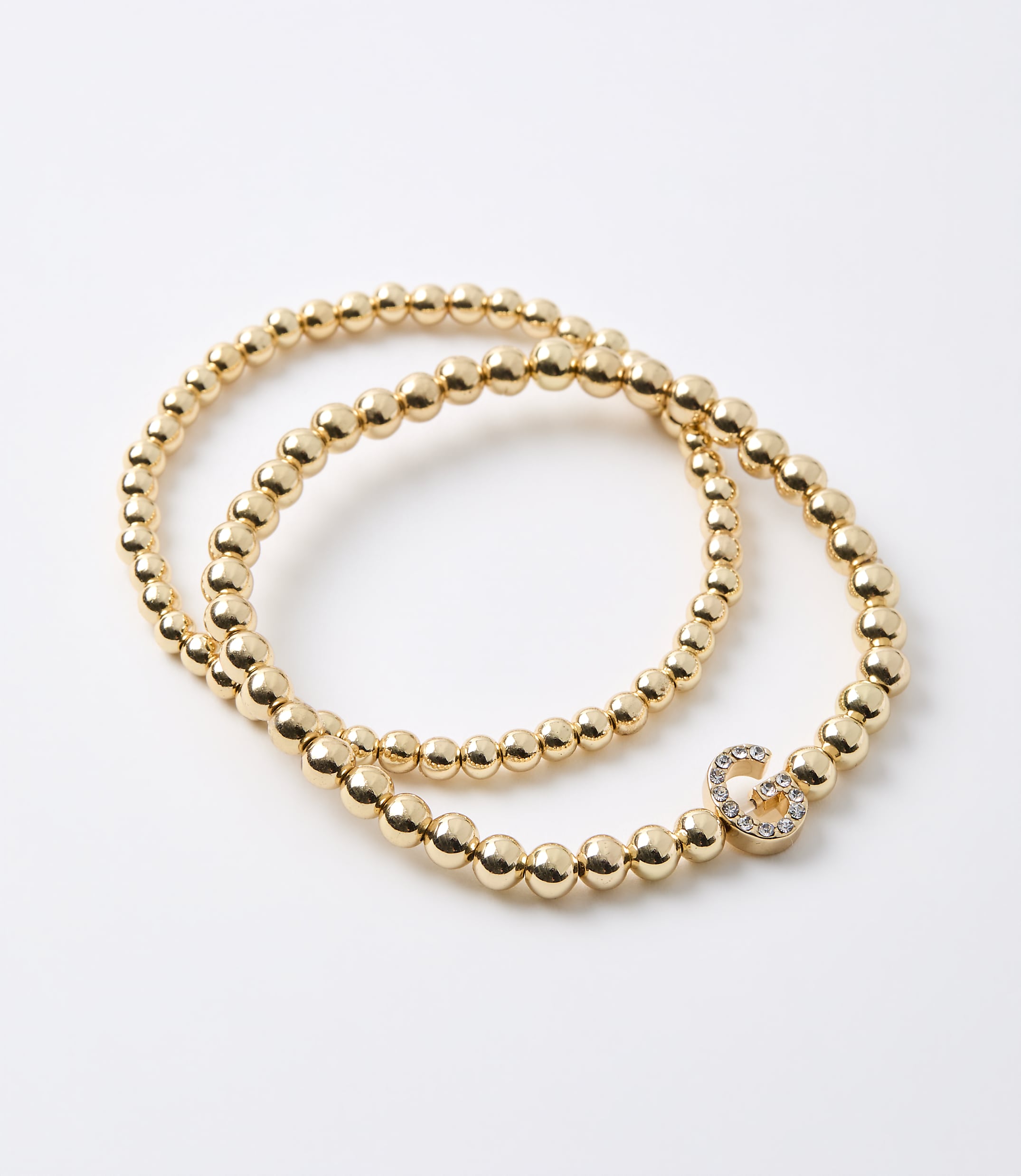 Two gold beaded bracelets, one with a diamond-encrusted infinity charm, lie on a plain white background.