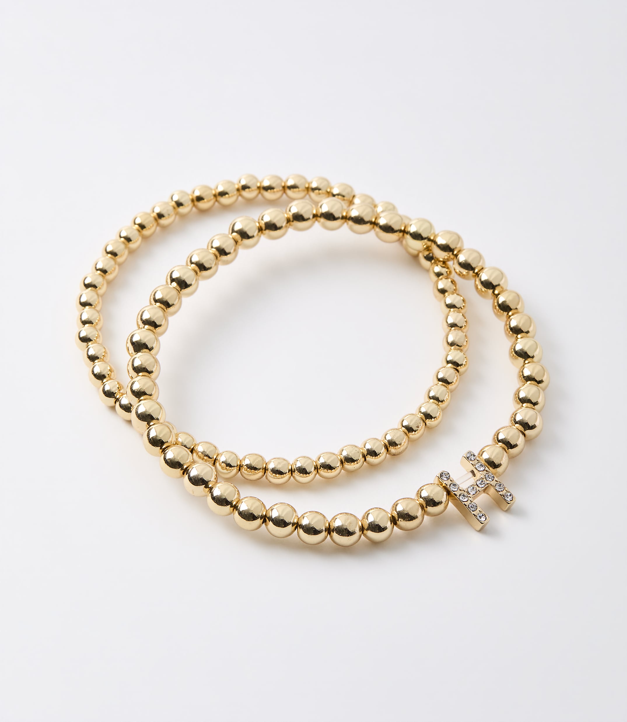 A gold beaded bracelet with a diamond-encrusted initial "H" rests on a plain white background.