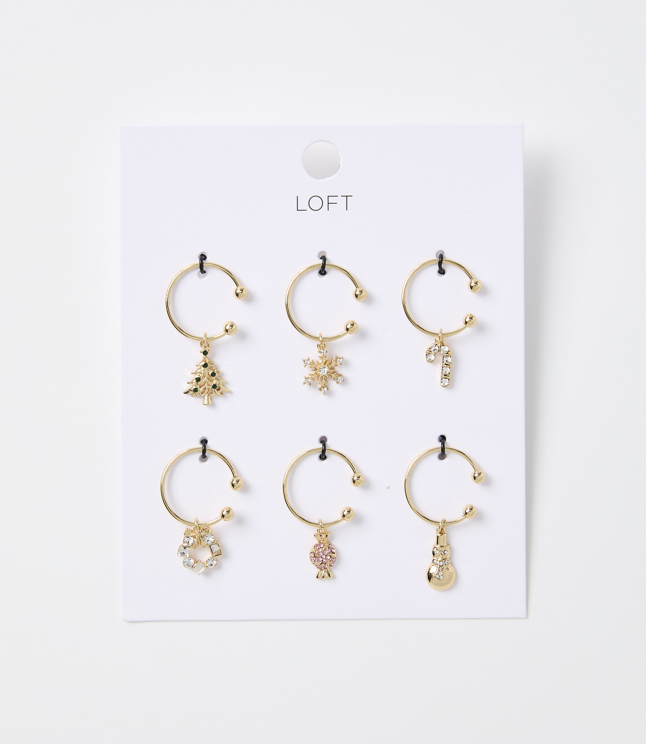 Six gold-toned hoop earrings with festive Christmas charms hang from a white card with the "LOFT" logo against a plain white background.