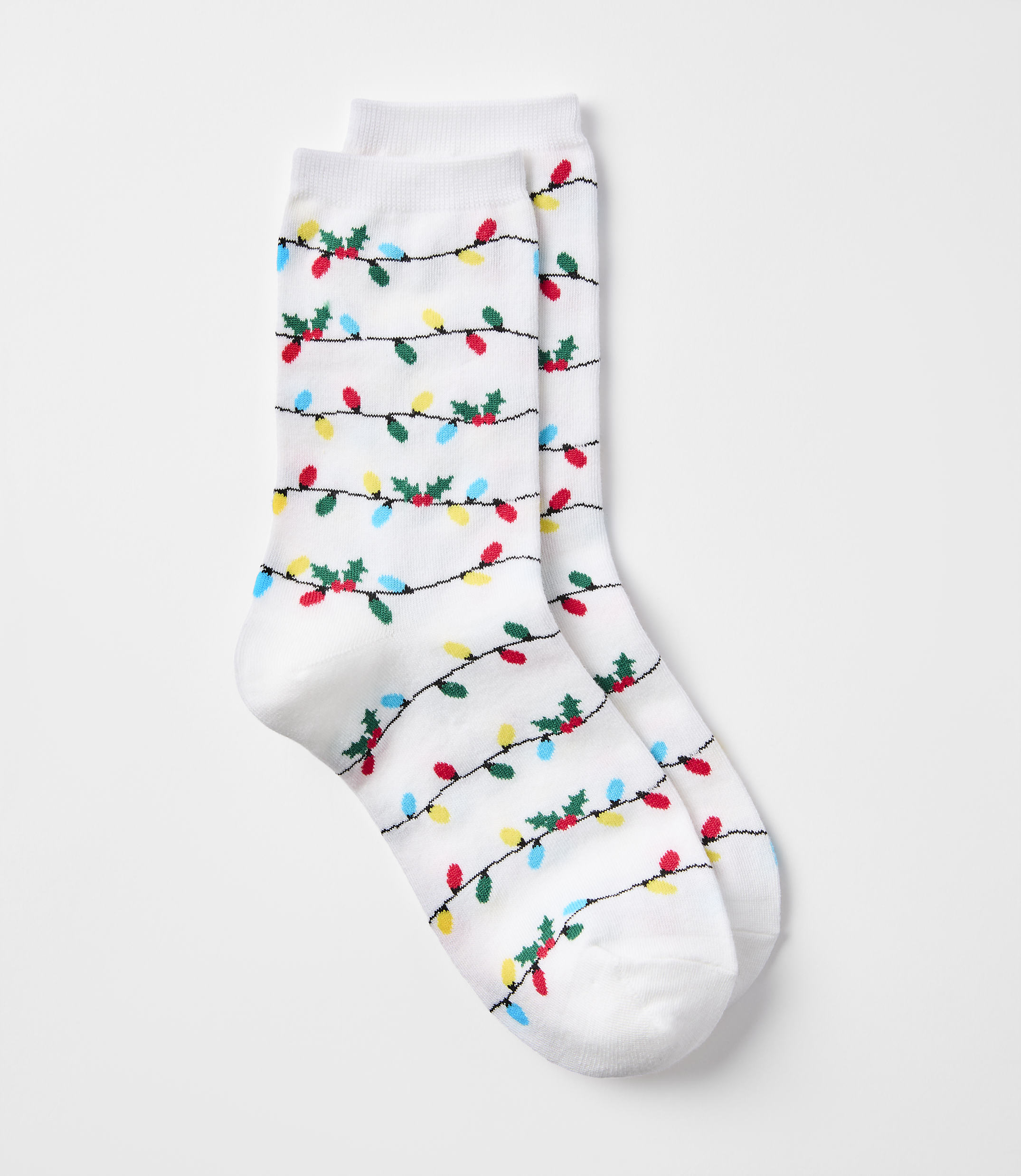 A pair of white socks with a pattern of colorful Christmas lights and holly adorns the foreground, set against a plain white background.