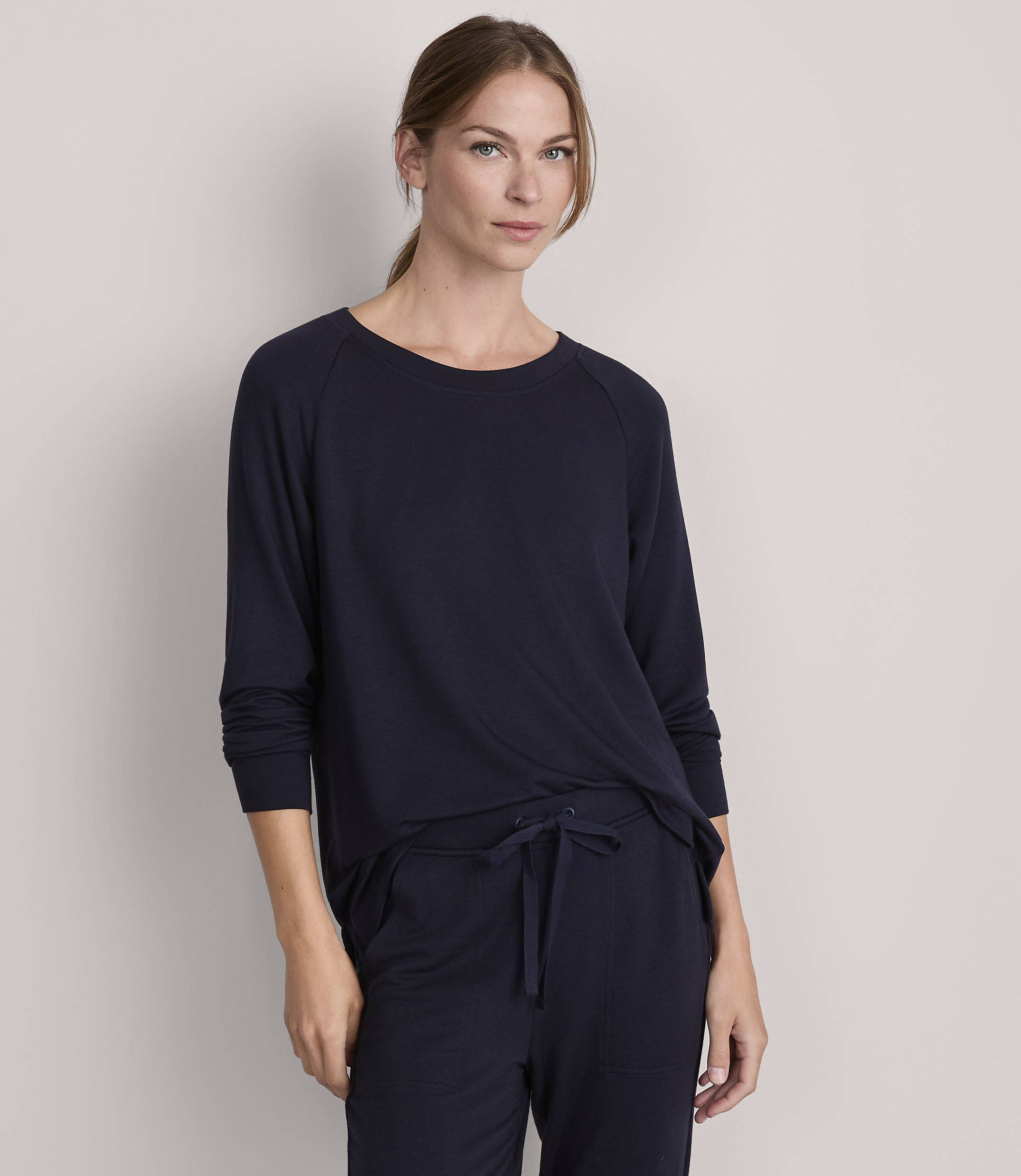A woman in a navy blue long-sleeved shirt and matching pants stands against a plain gray background.
